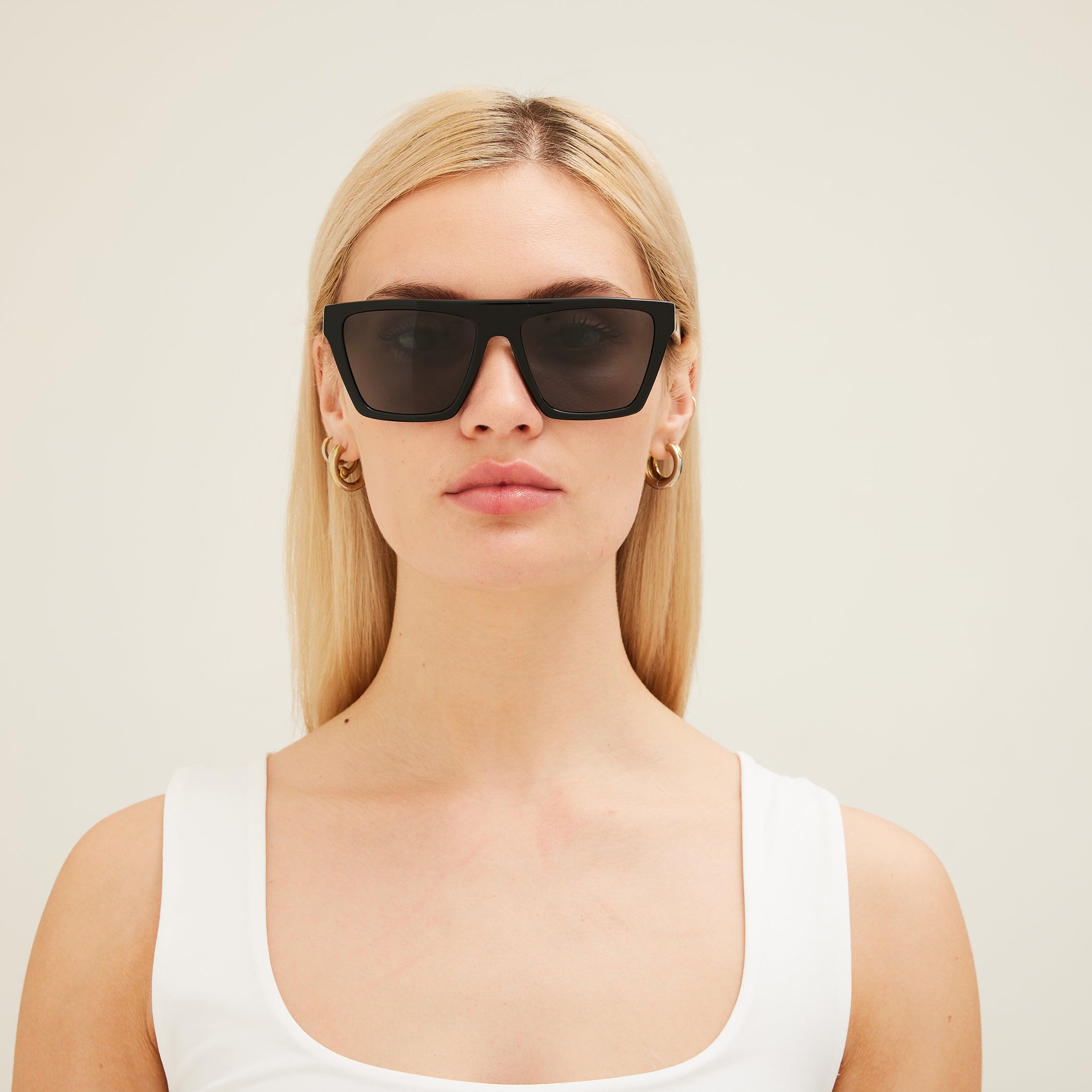 Woman wearing black sunglasses and a white top against a plain background