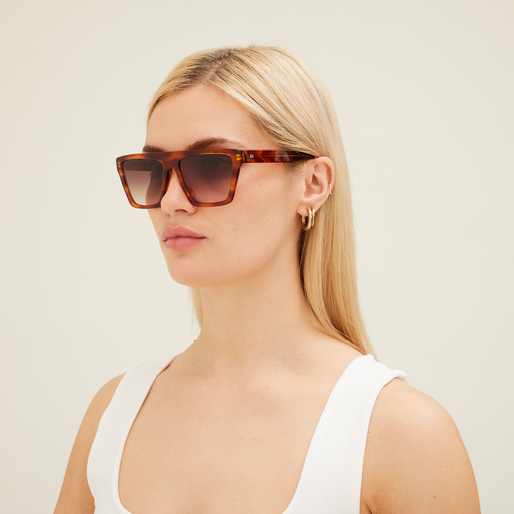 Woman wearing tortoiseshell sunglasses with a plain background