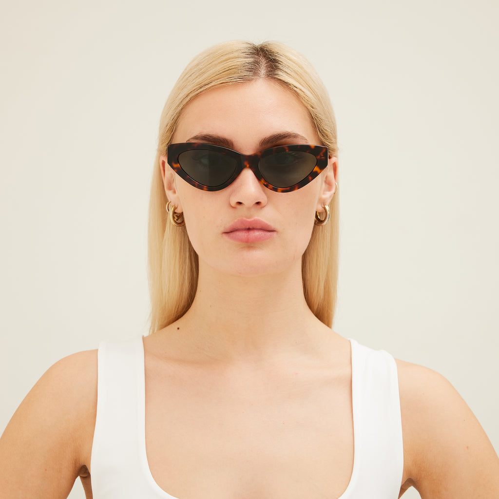 Woman wearing cat-eye sunglasses with tortoiseshell frame and dark lenses on a white background