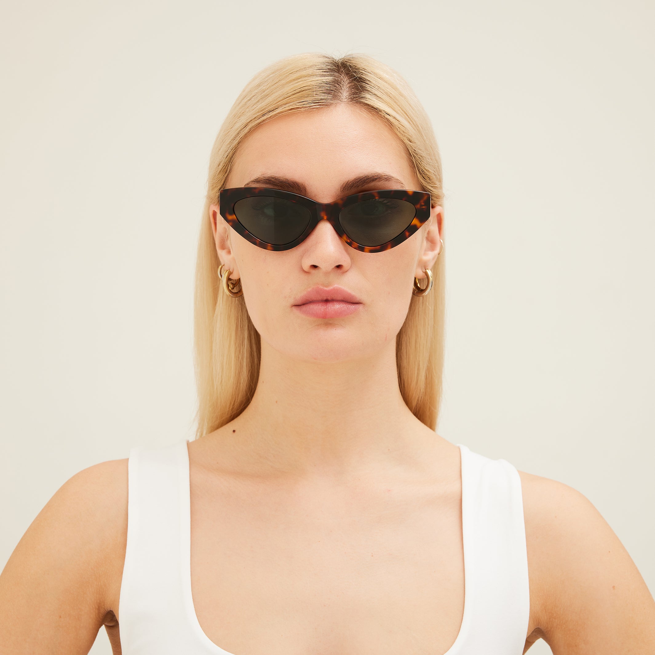 Woman wearing cat-eye sunglasses with tortoiseshell frame and dark lenses on a white background
