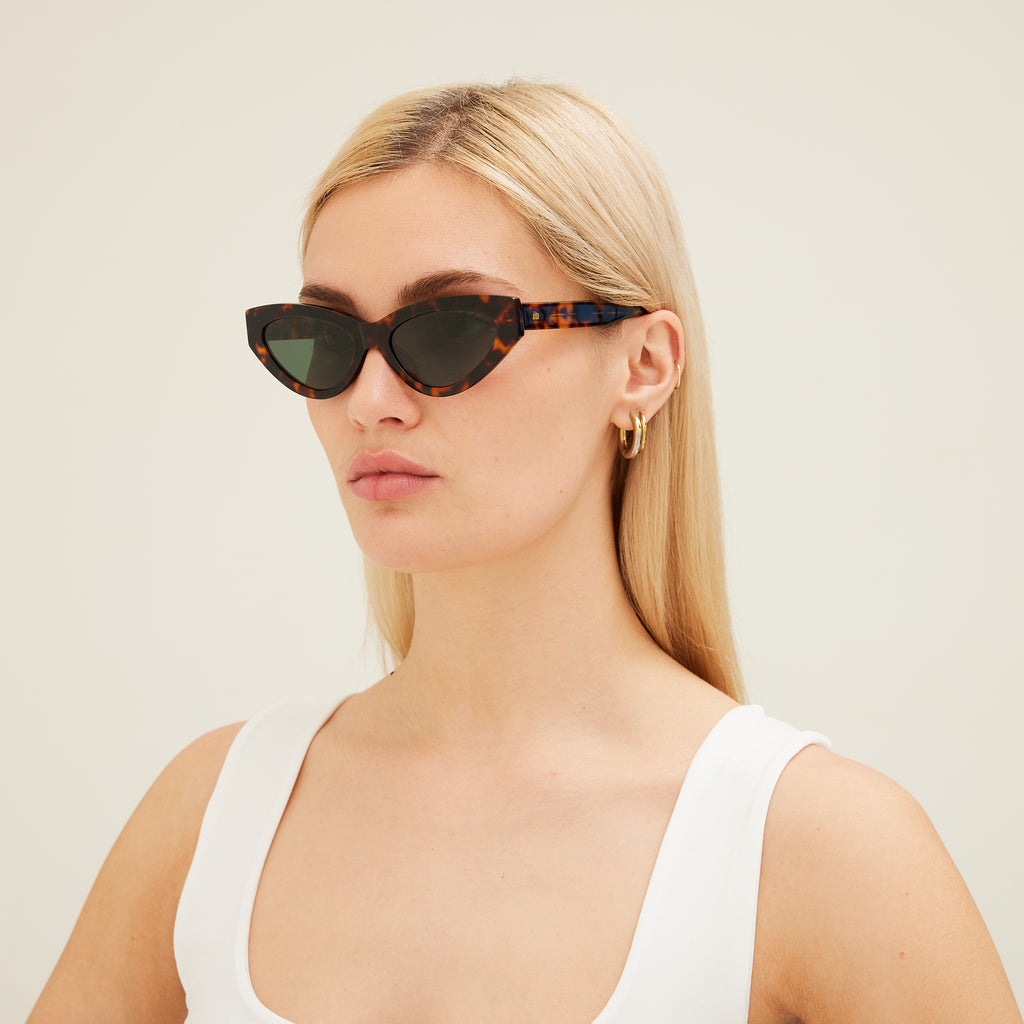 Woman wearing cat-eye sunglasses with tortoiseshell frame and dark lenses on a white background