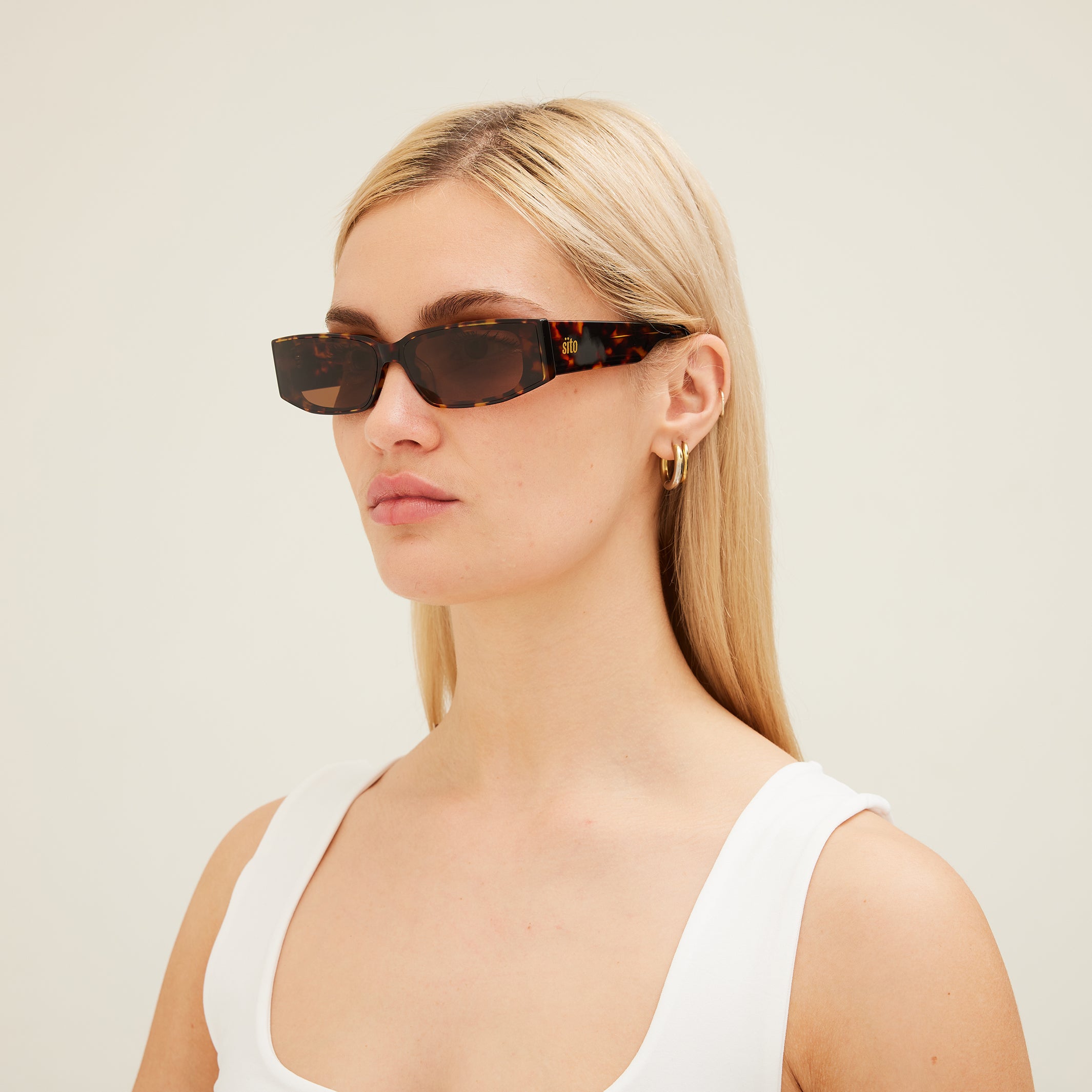 Woman wearing tortoiseshell sunglasses with a neutral background