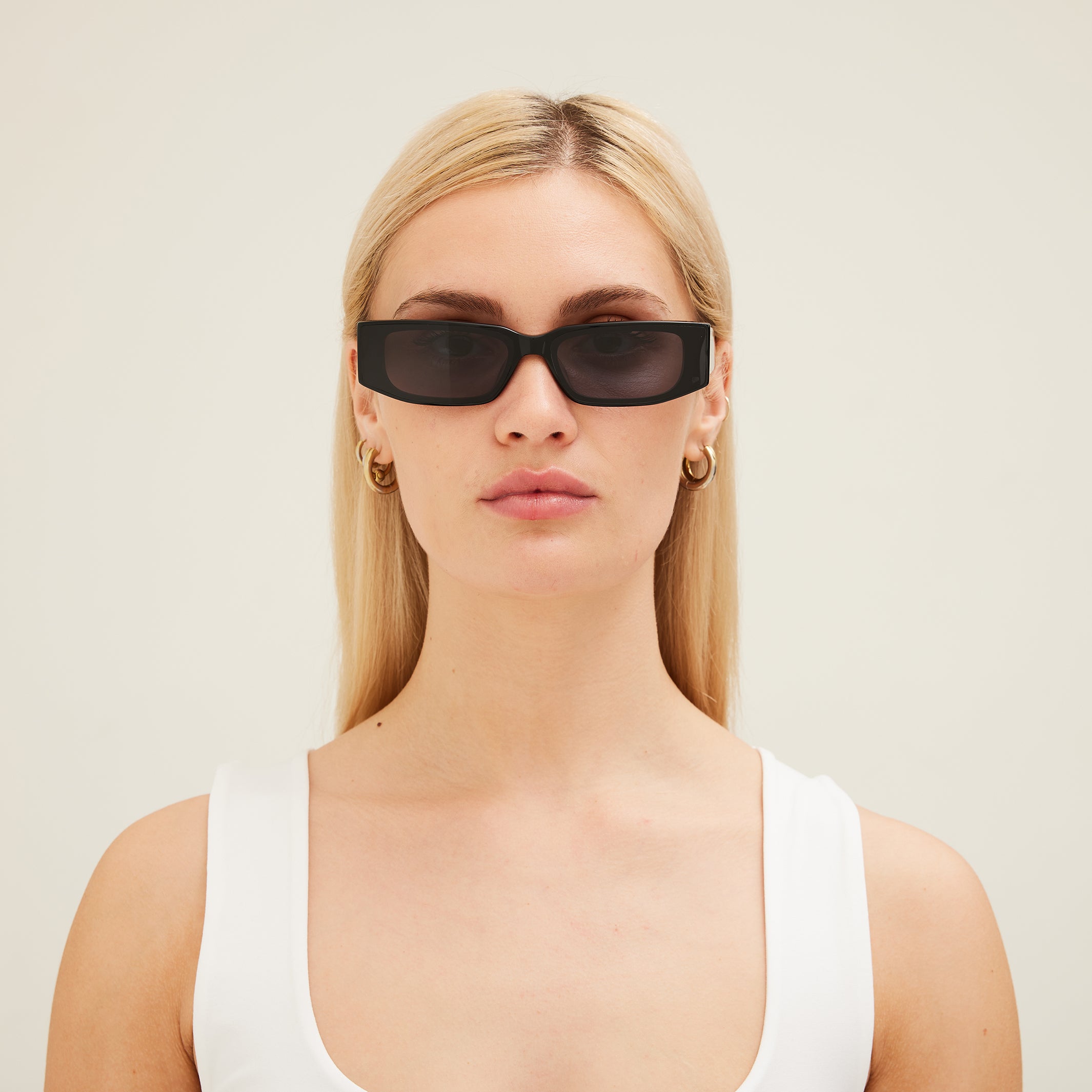 Woman wearing black sunglasses and a white top against a light background