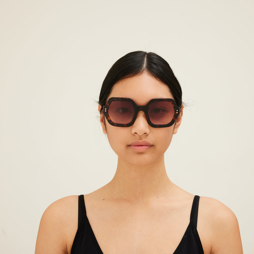 Woman wearing sunglasses with tortoiseshell frame and gradient lenses on a white background. 