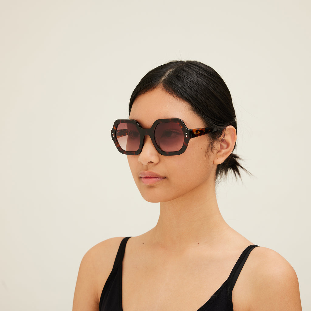 Woman wearing sunglasses with tortoiseshell frame and gradient lenses on a white background. 