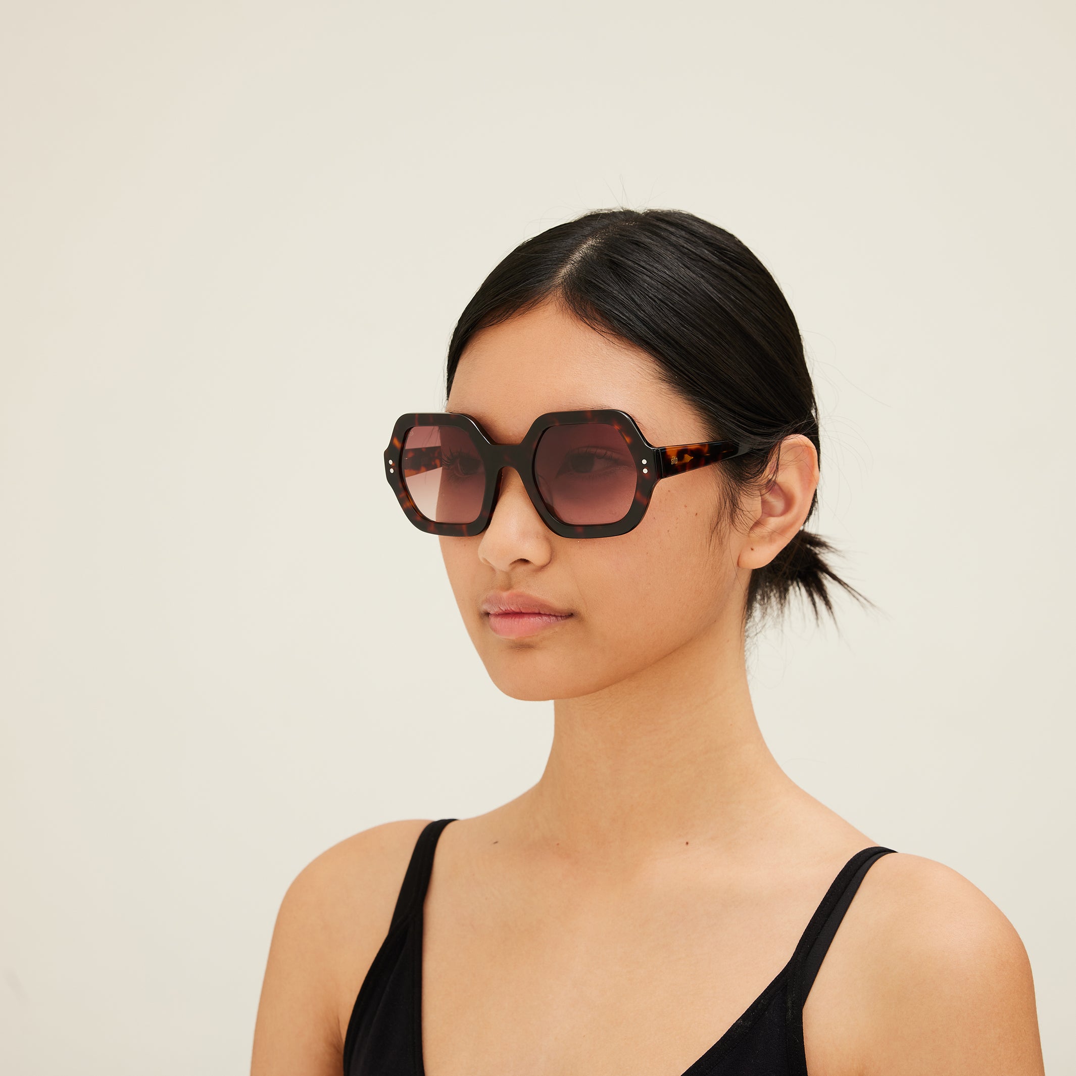 Woman wearing sunglasses with tortoiseshell frame and gradient lenses on a white background. 