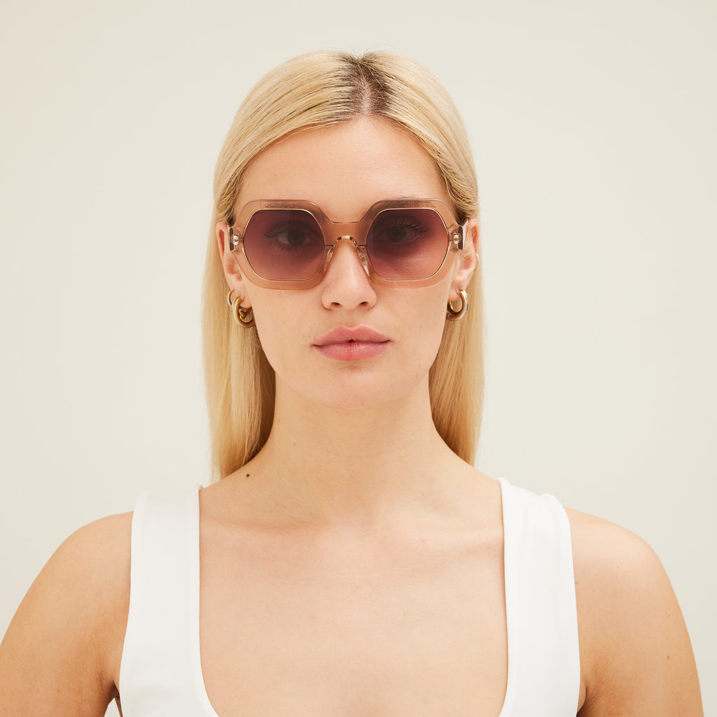Woman wearing pink sunglasses with gradient lenses on a white background