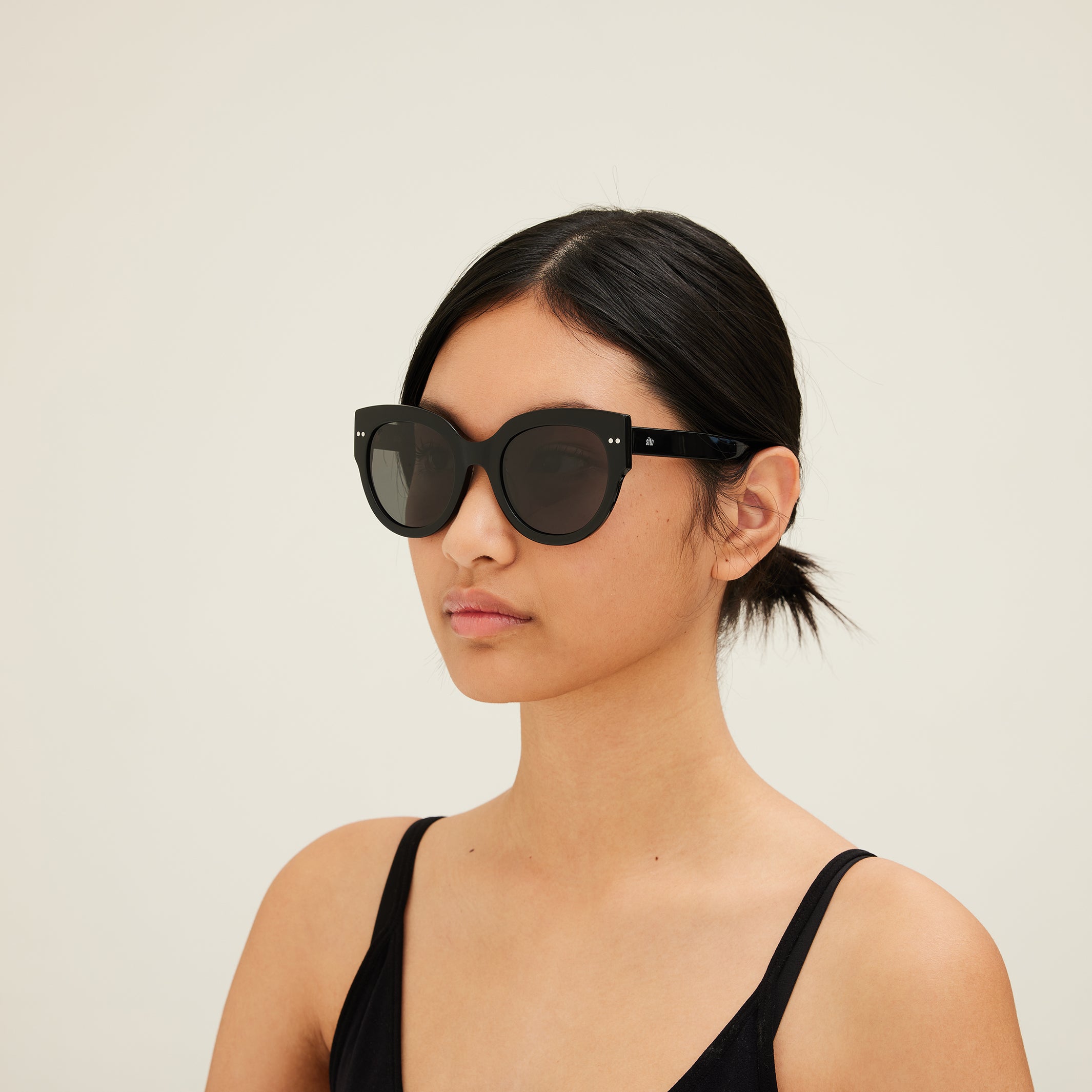 Woman wearing black sunglasses with dark lenses on a white background