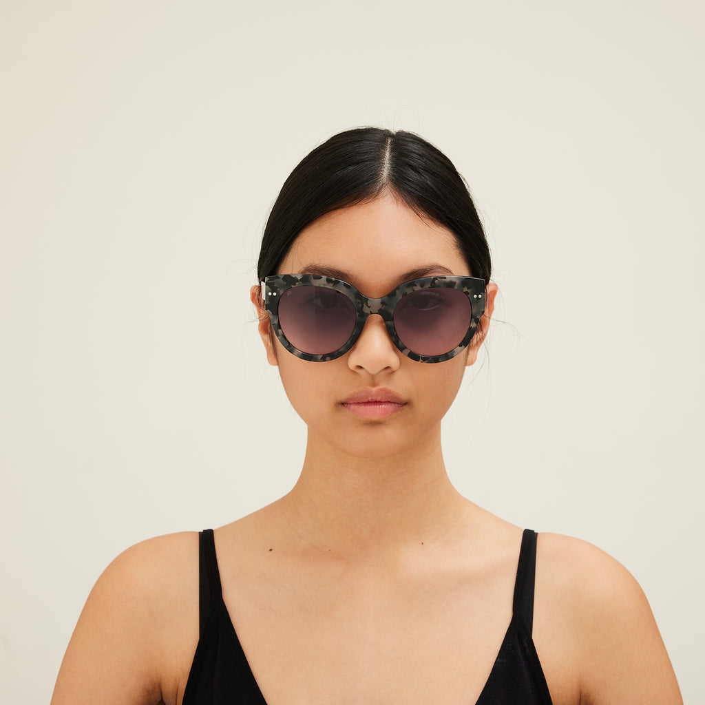 Woman wearing sunglasses with tortoiseshell frame and gray lenses on a white background