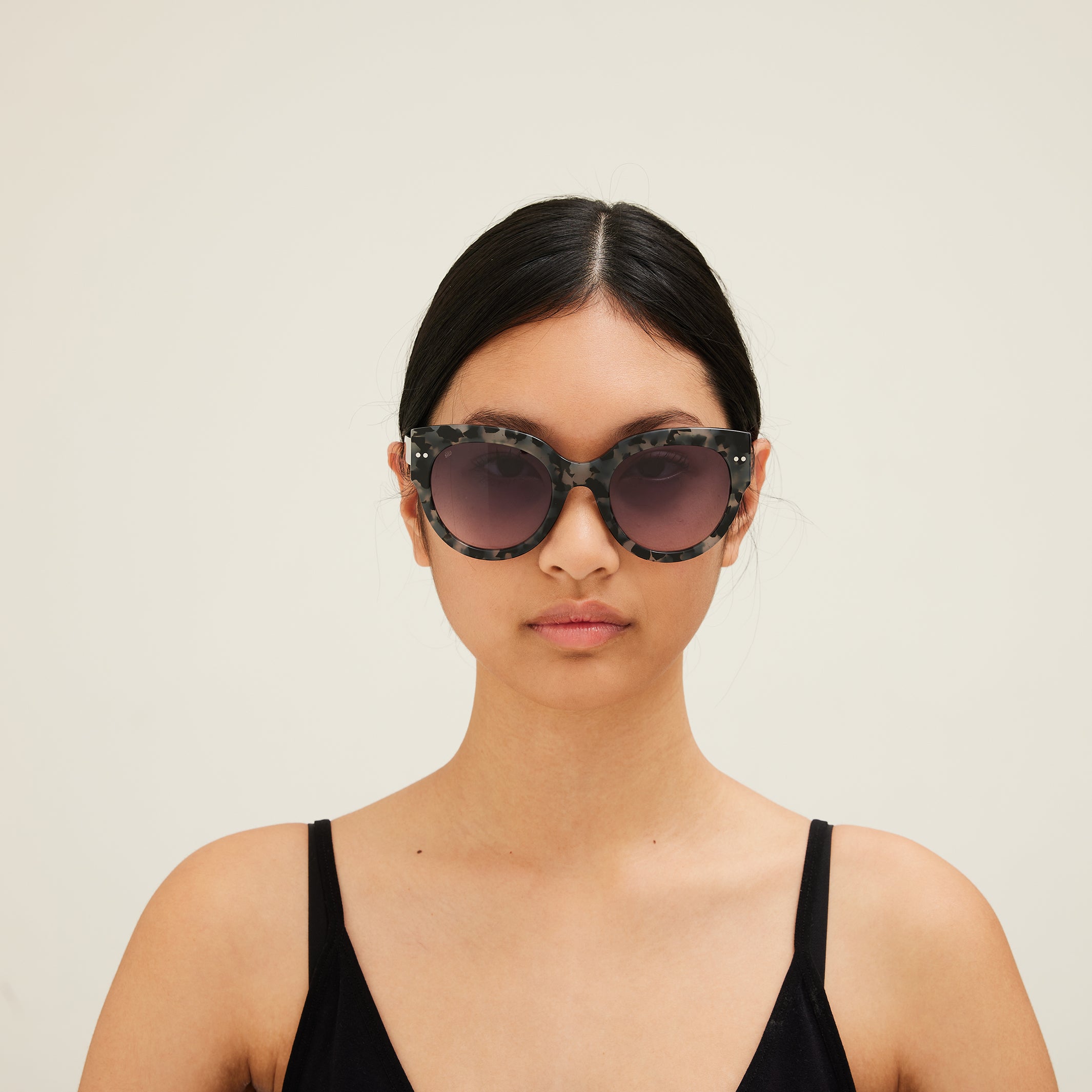 Woman wearing sunglasses with tortoiseshell frame and gray lenses on a white background