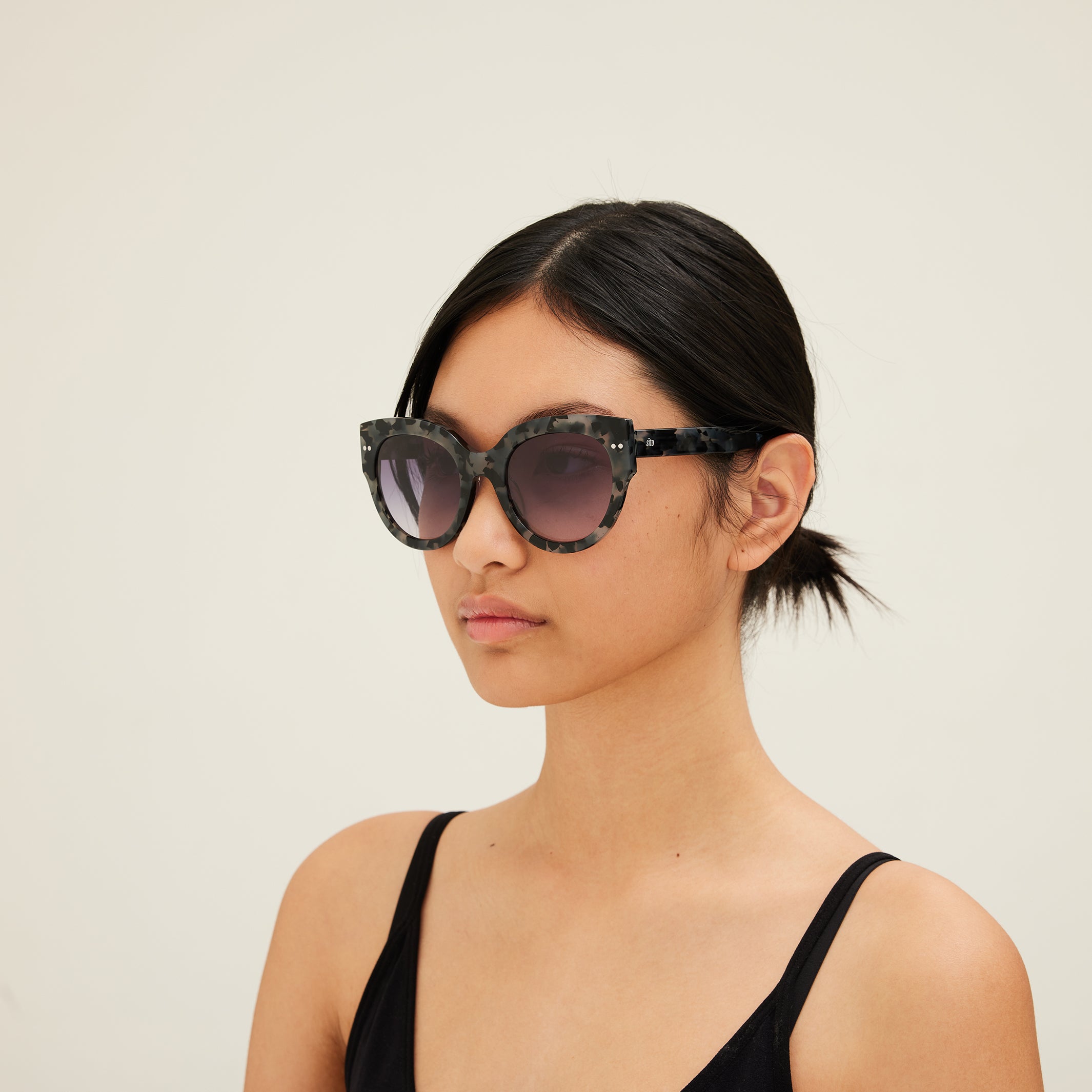 Woman wearing sunglasses with tortoiseshell frame and gray lenses on a white background