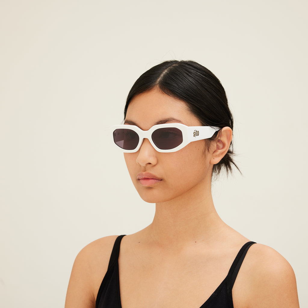 Woman wearing white sunglasses with a neutral background
