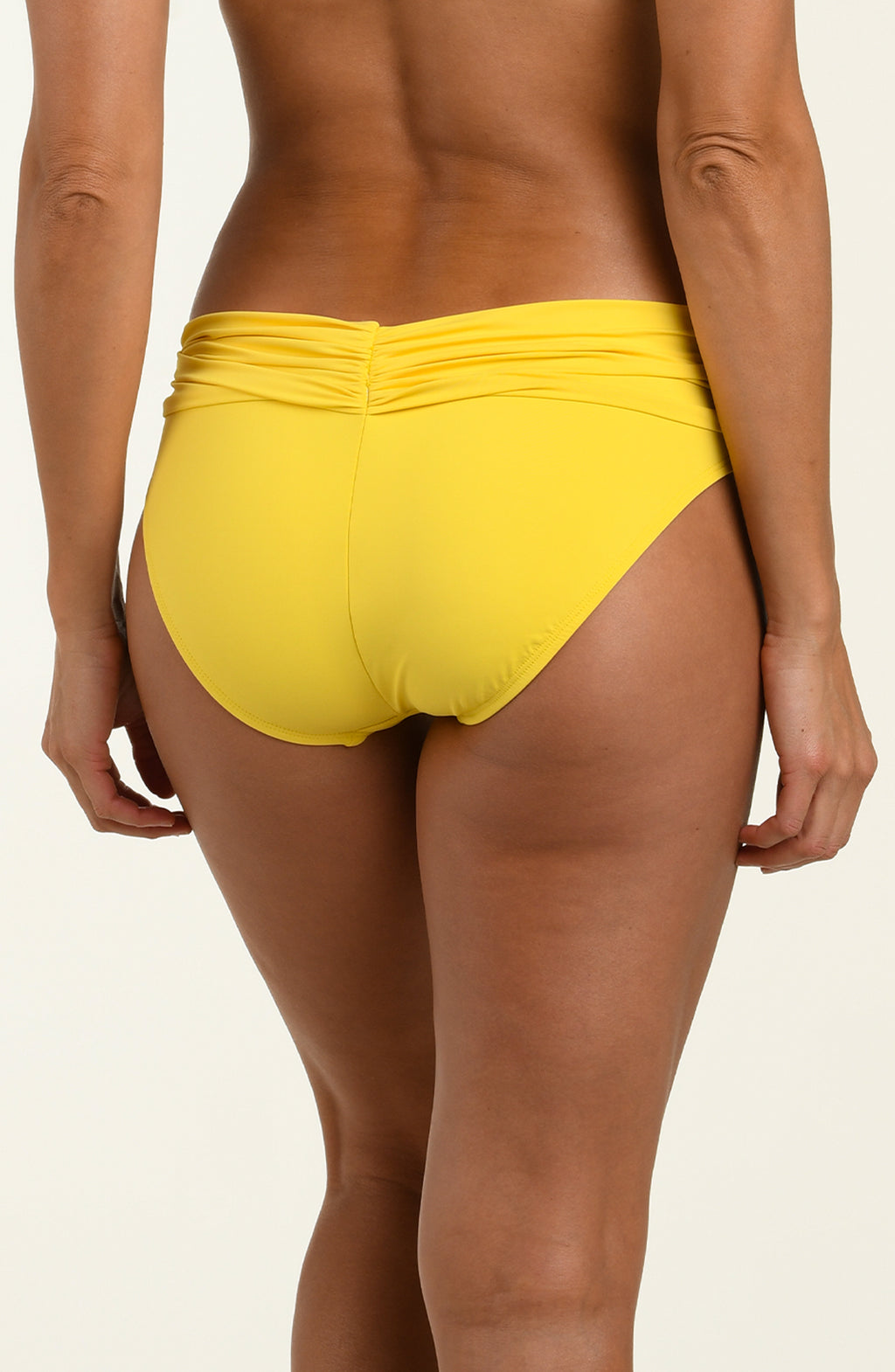 Woman wearing a yellow bikini bottom against a white background.