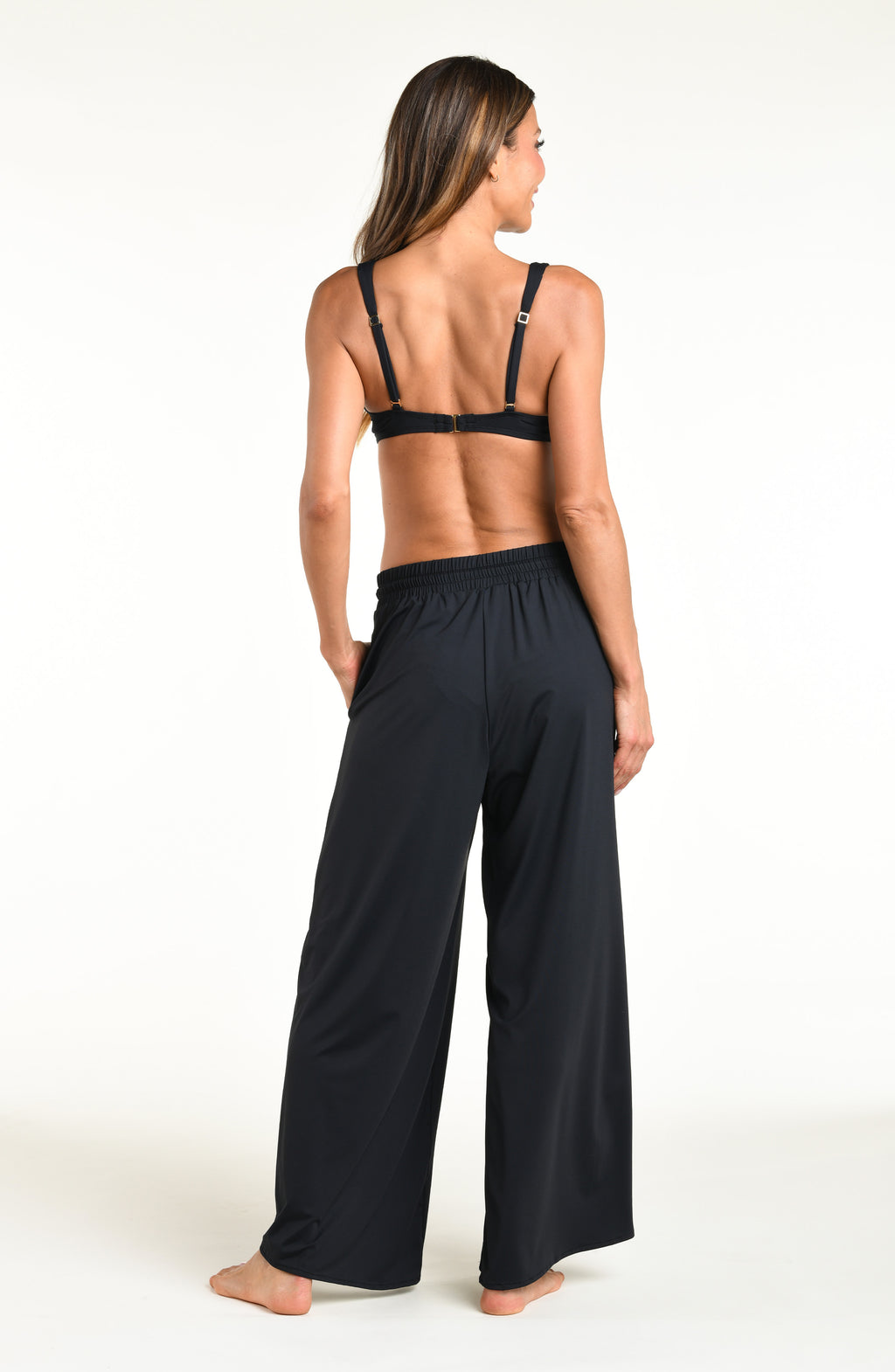 Woman wearing solid black bikini top and matching pants against a white background. 