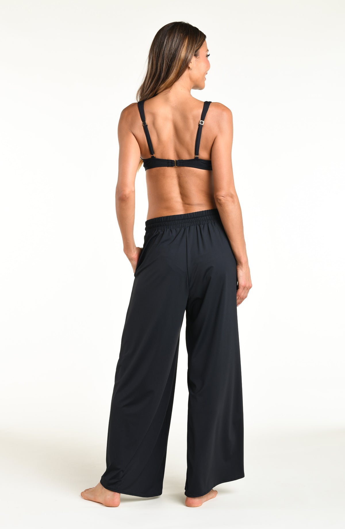 Woman wearing solid black bikini top and matching pants against a white background. 