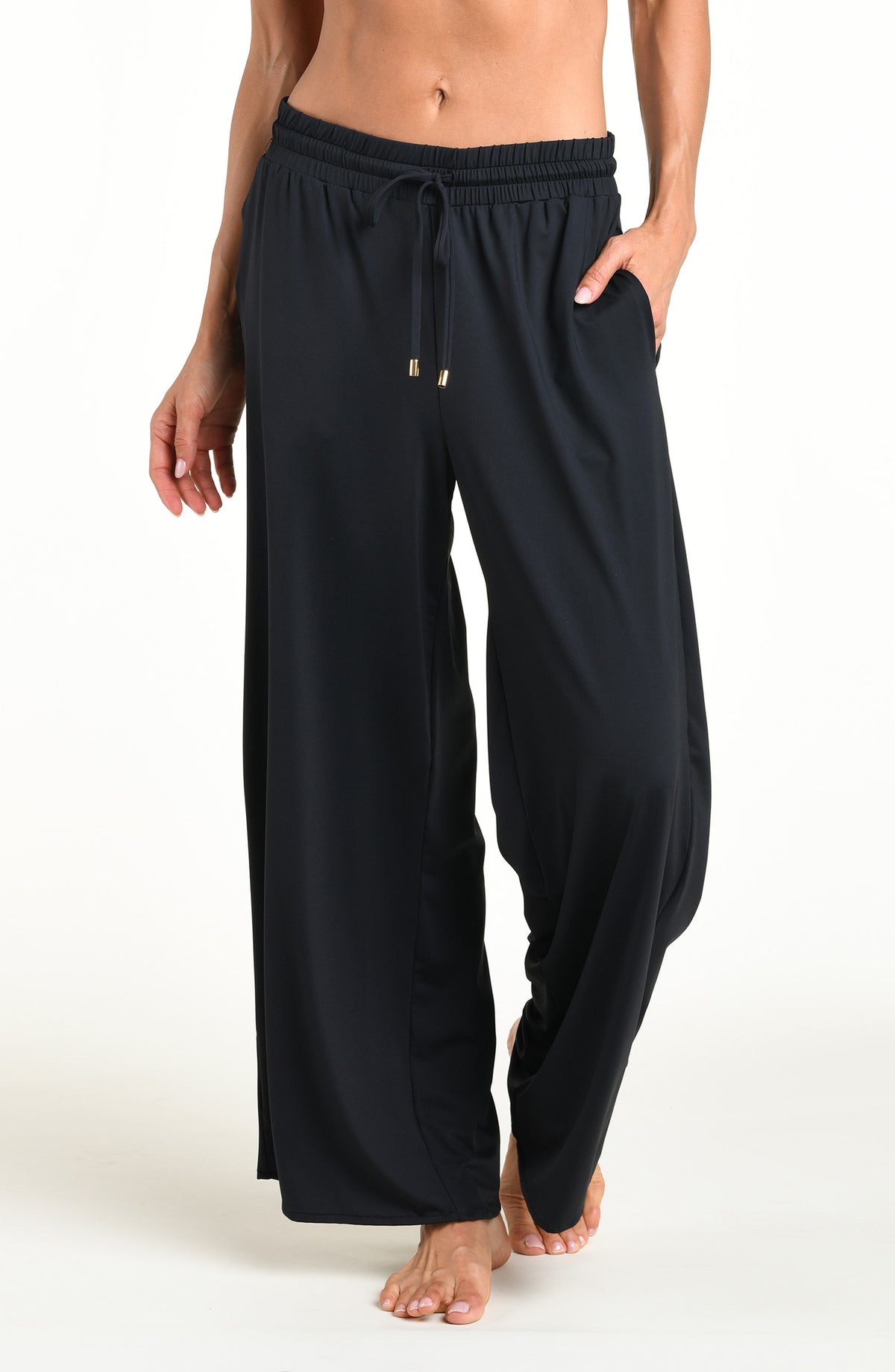 Woman wearing solid black beach pants against a white background. 