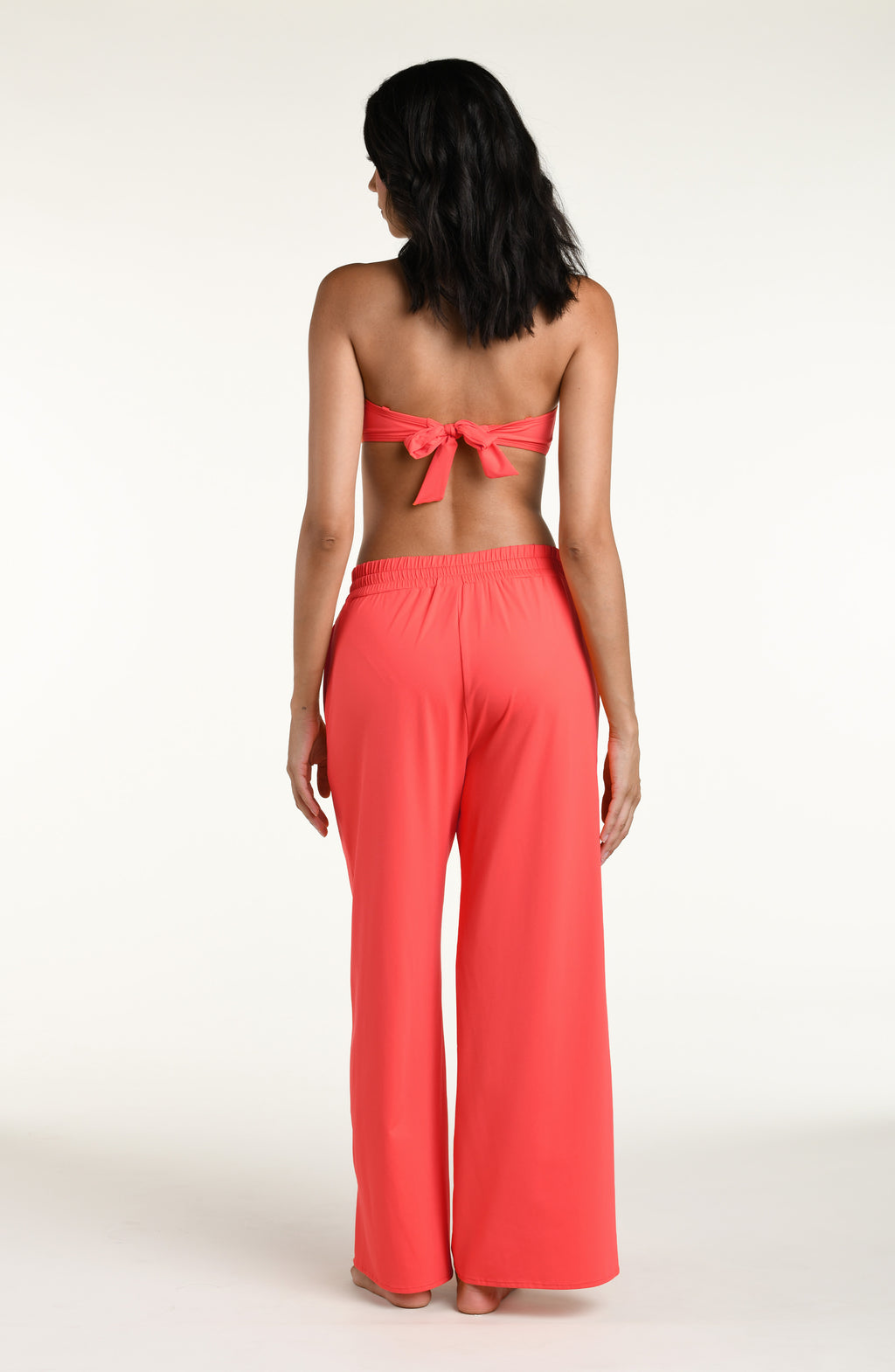 Woman wearing a bright orange bandeau bikini top and matching beach pants against a white background. 