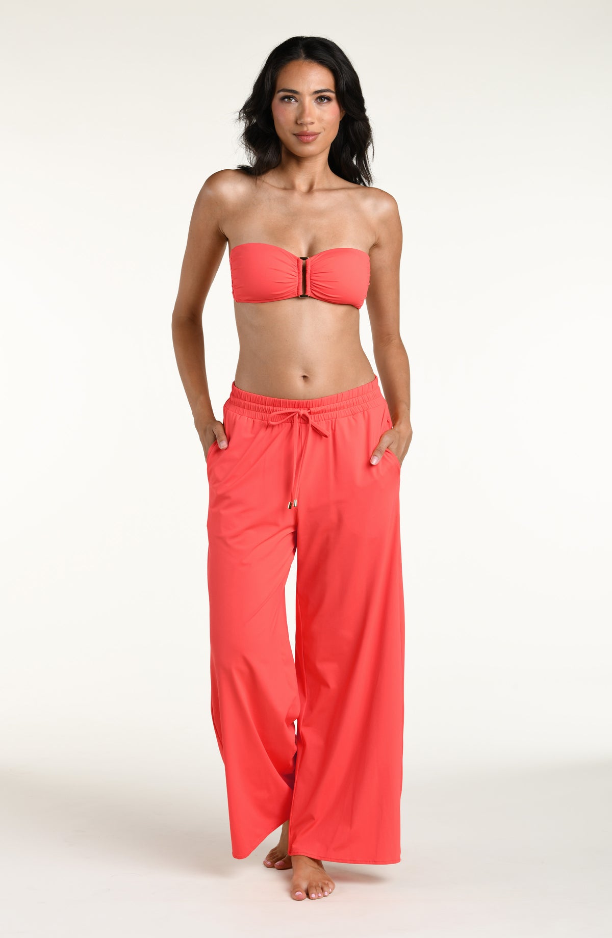 Woman wearing a bright orange bandeau bikini top and matching beach pants against a white background. 