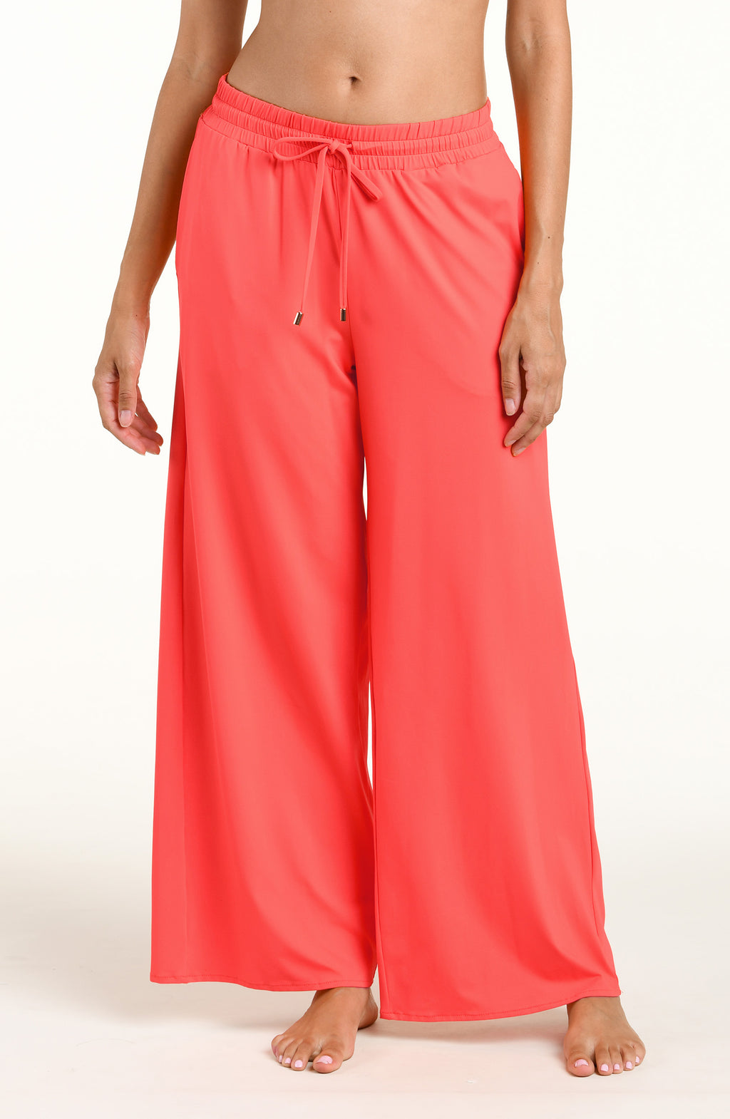 Woman wearing bright orange beach pants against a white background. 