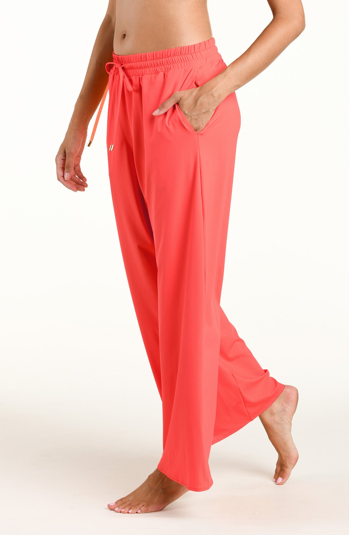 Woman wearing bright orange beach pants against a white background. 