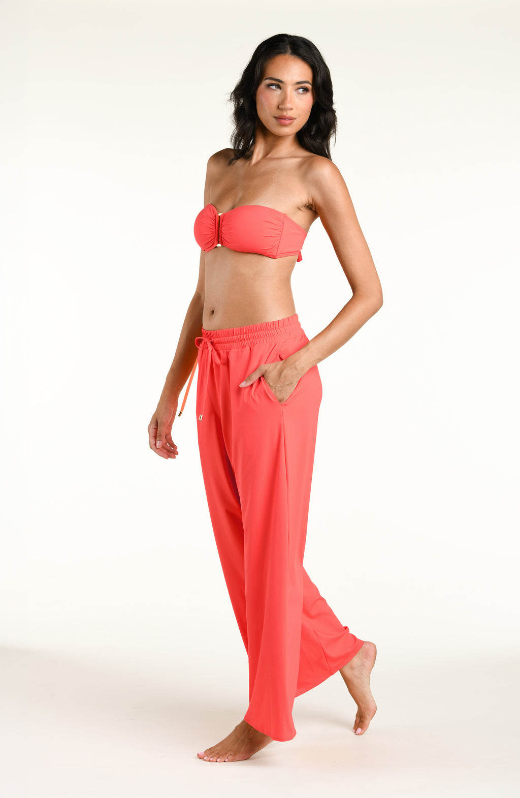 Woman wearing a bright orange bandeau bikini top and matching beach pants against a white background. 
