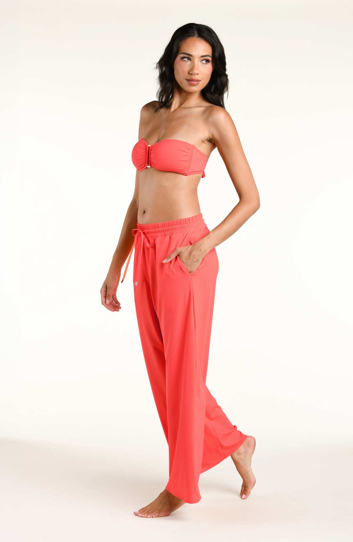 Woman wearing a bright orange bandeau bikini top and matching beach pants against a white background. 