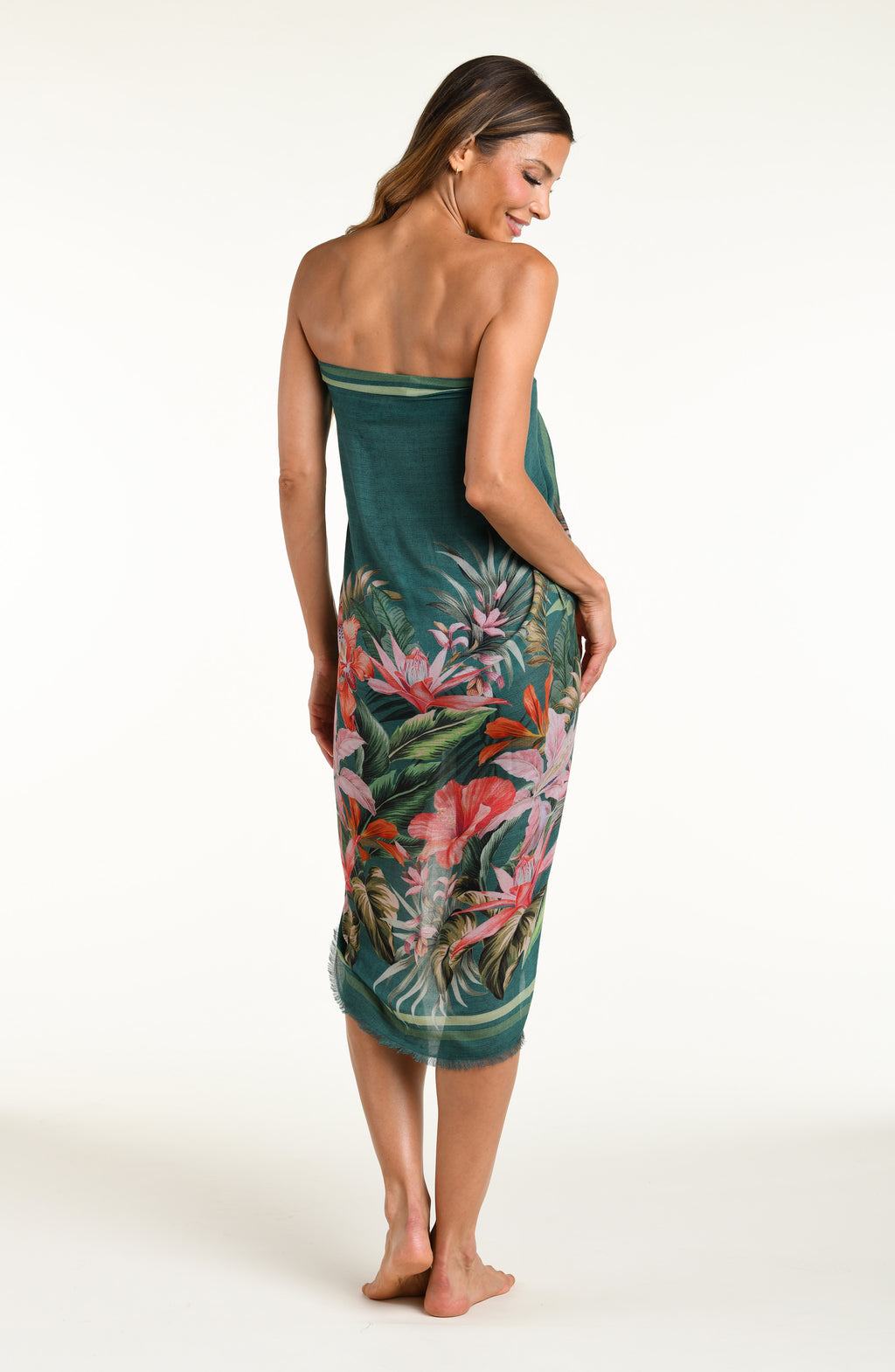 A model wearing a dark teal green tropical printed canga wrap skirt with a side slit, shown from the waist down against a white background.