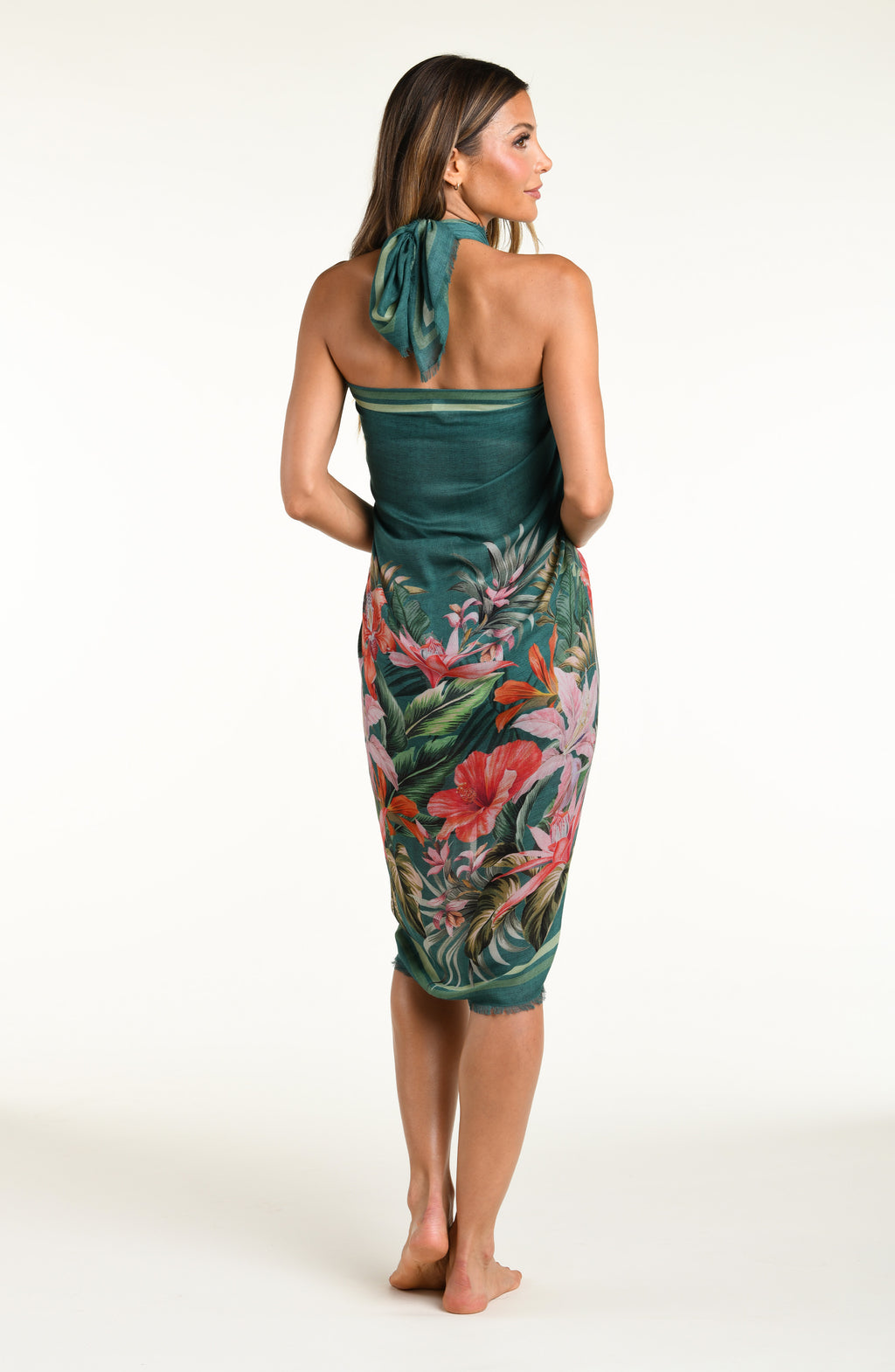 A model wearing a dark teal green tropical printed canga wrap skirt with a side slit, shown from the waist down against a white background.