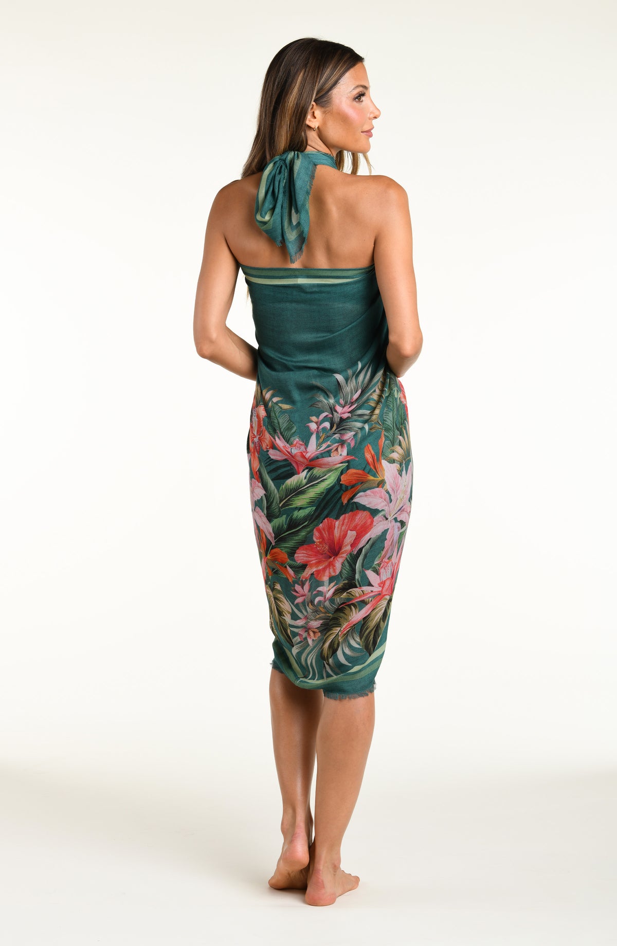 A model wearing a dark teal green tropical printed canga wrap skirt with a side slit, shown from the waist down against a white background.