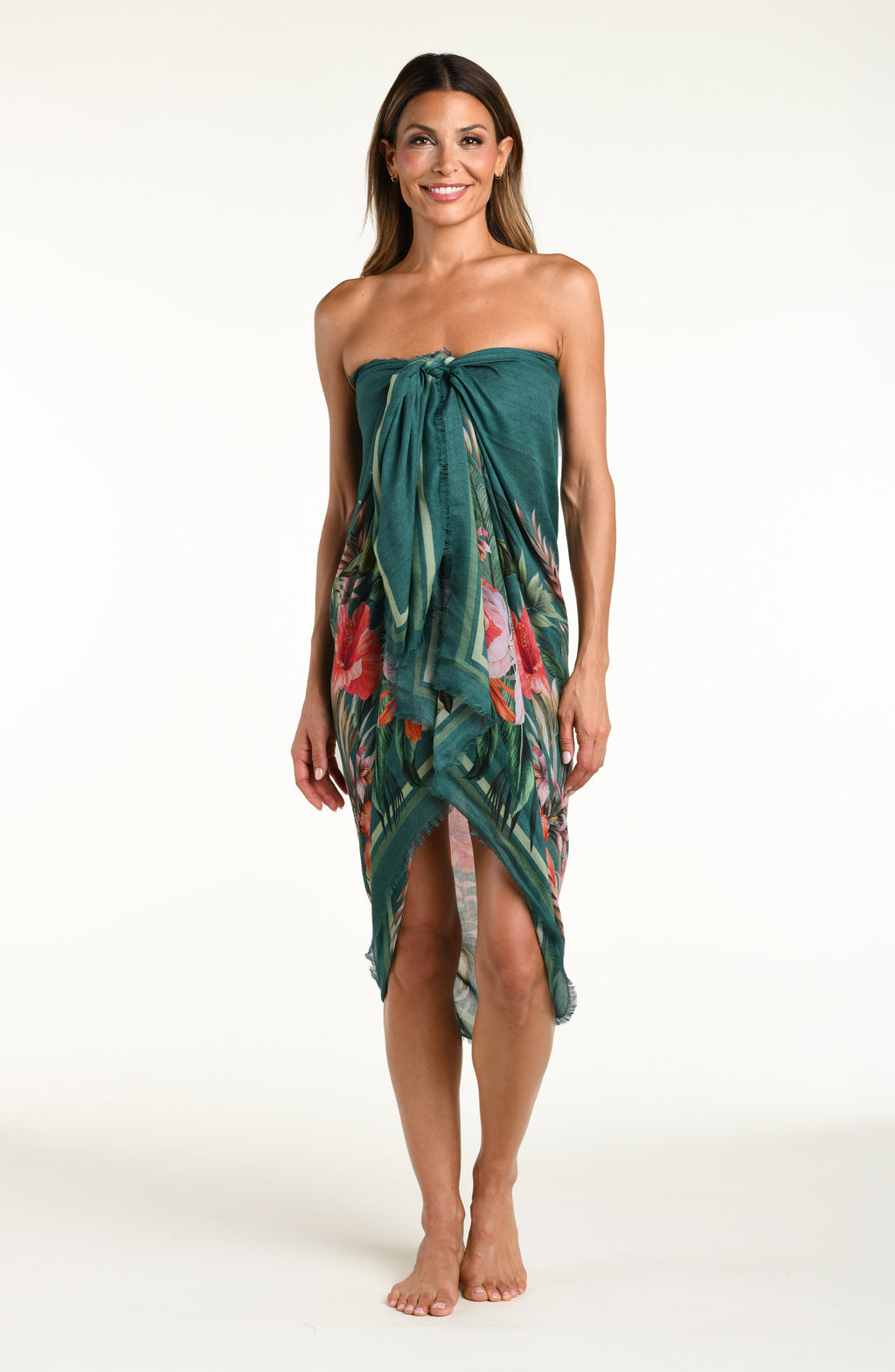 A model wearing a dark teal green tropical printed canga wrap skirt with a side slit, shown from the waist down against a white background.