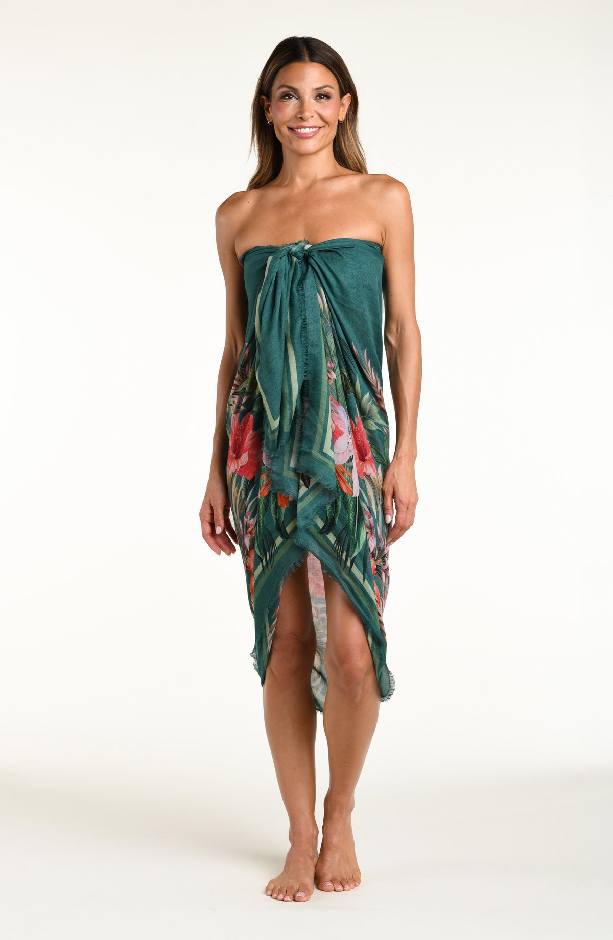 A model wearing a dark teal green tropical printed canga wrap skirt with a side slit, shown from the waist down against a white background.