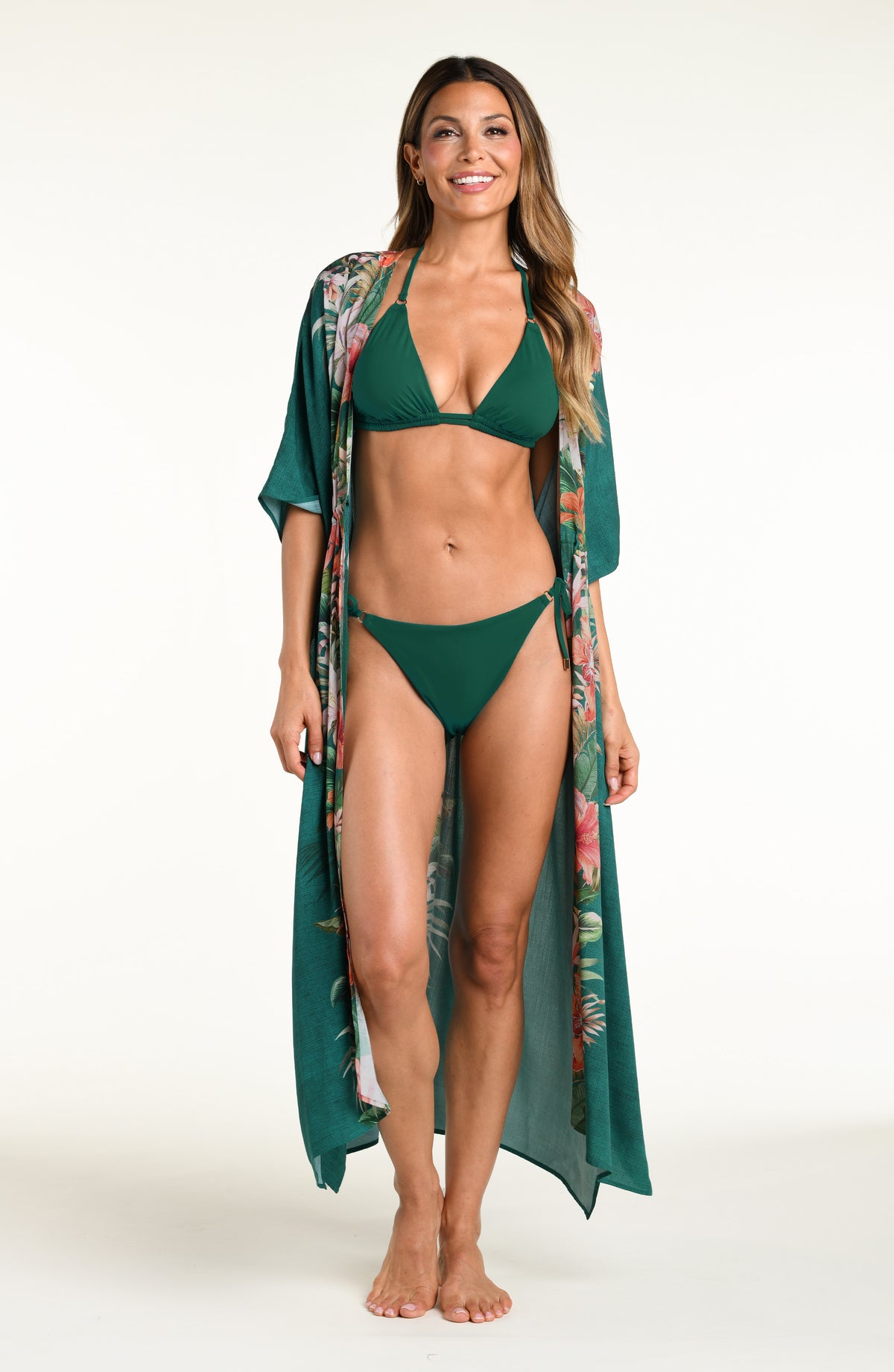 Woman wearing a jungle green bikini top and matching bottom under a multicolored long kimono against a white background. 