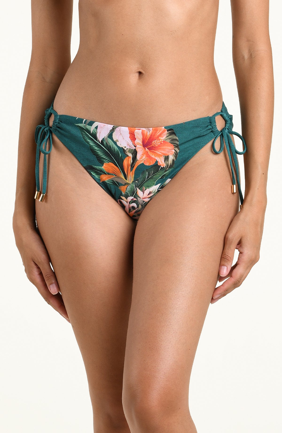 A model wearing teal bikini bottoms with a vibrant orange, pink, and green tropical floral print, featuring side-tie details.