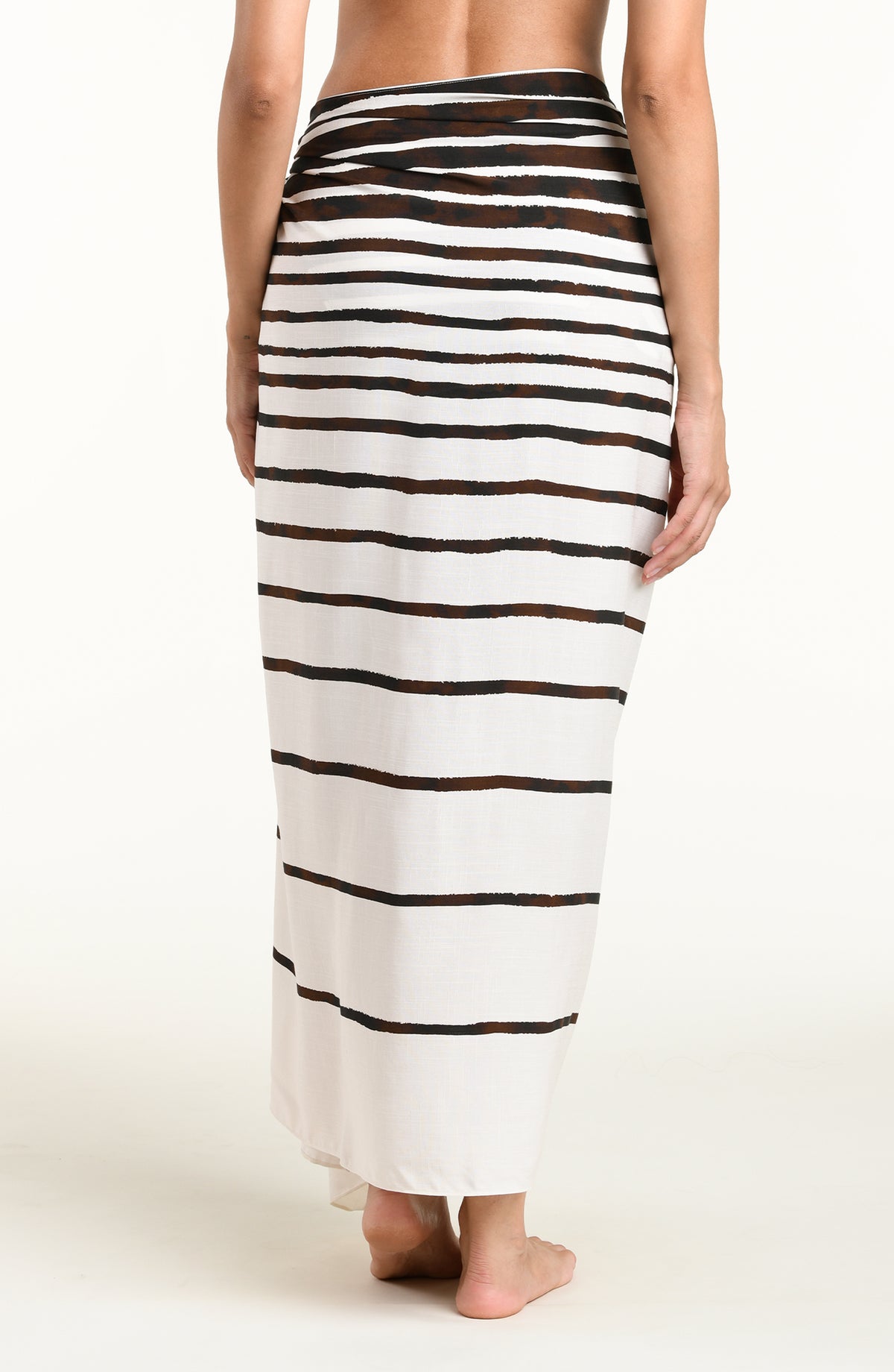 A woman wearing a brown and white striped wrap sarong skirt against a plain light background.