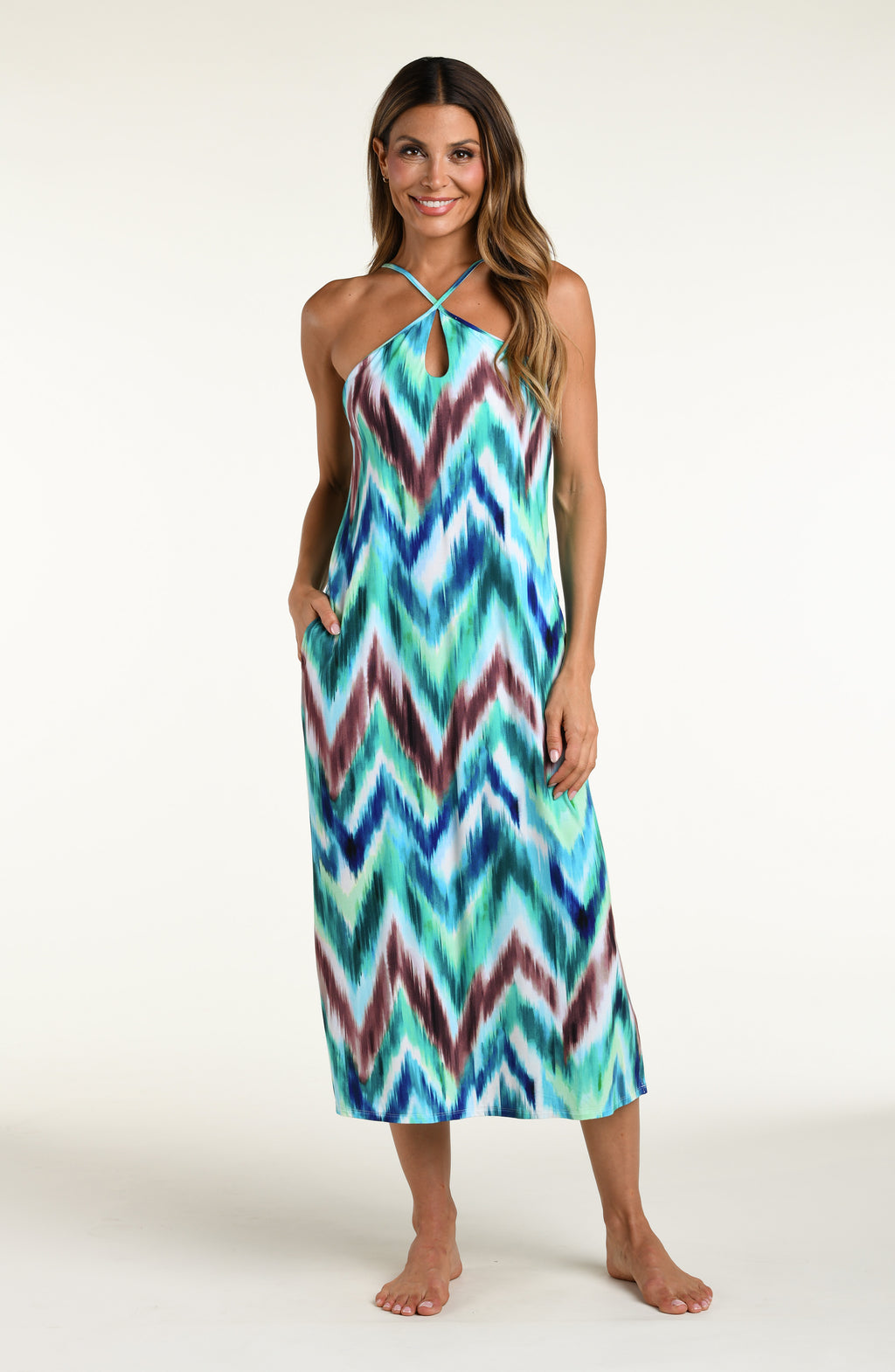 Woman wearing a multicolored teal midi dress cover up against a white background. 