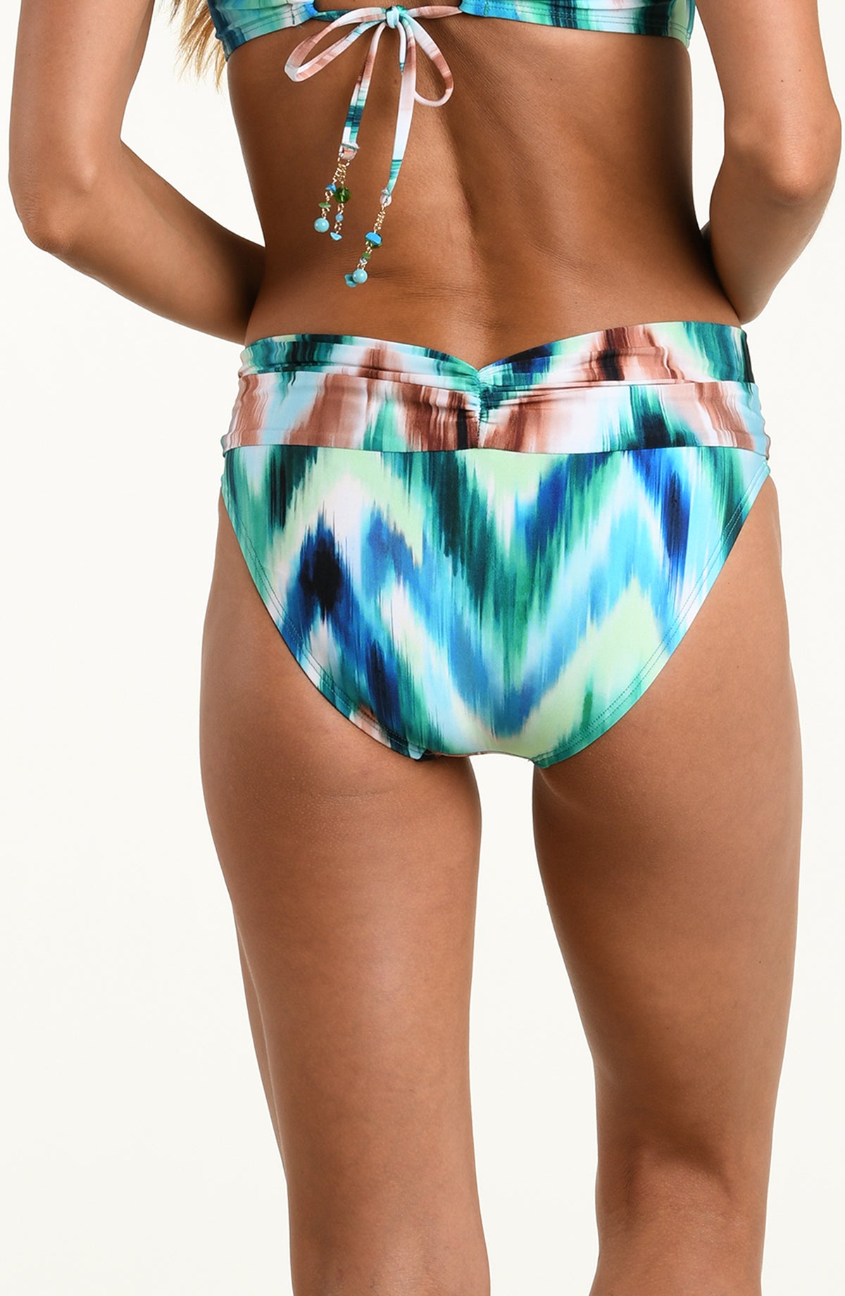 Woman wearing a multicolored teal bikini bottom against a white background. 