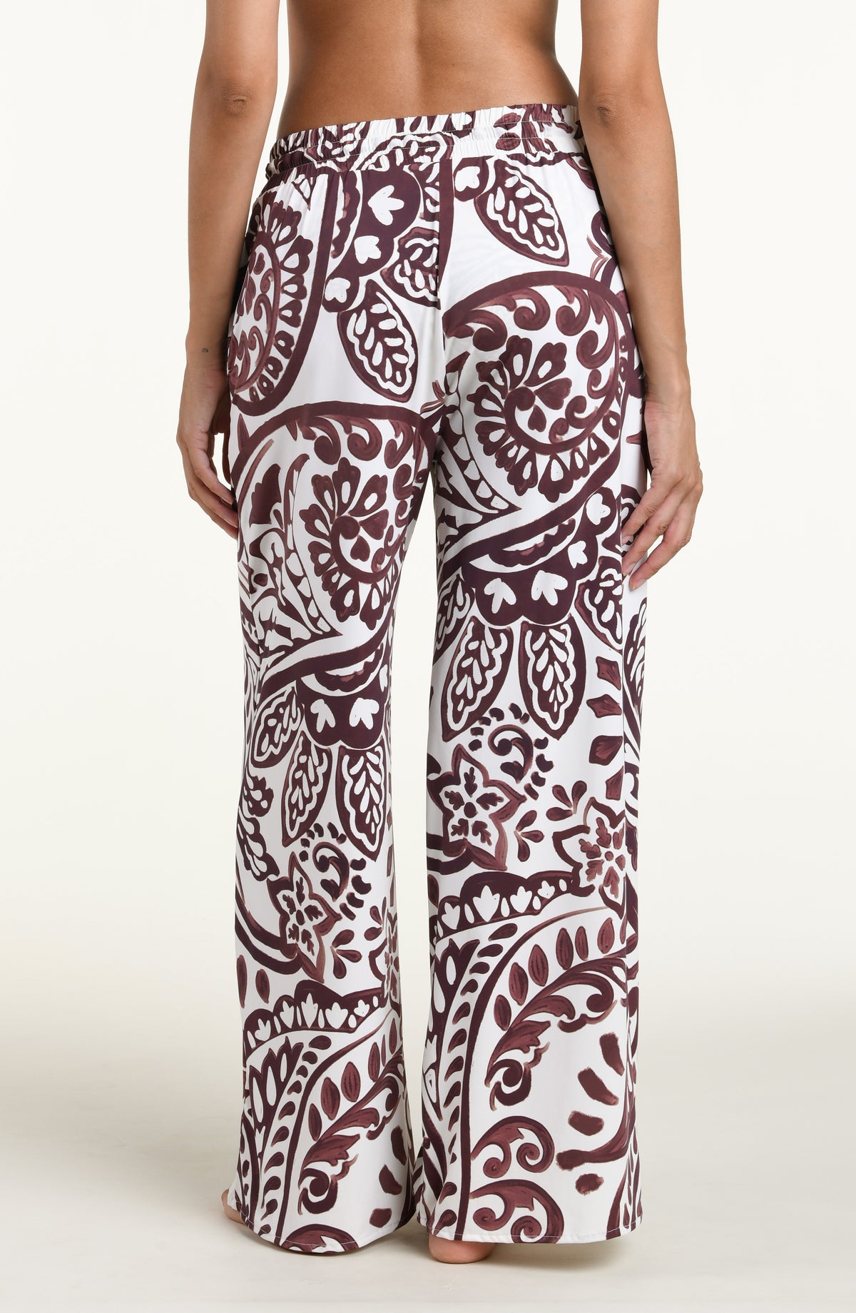 A person wearing loose, wide-leg pants with an allover paisley-style print in dark brown and white against a plain light background.