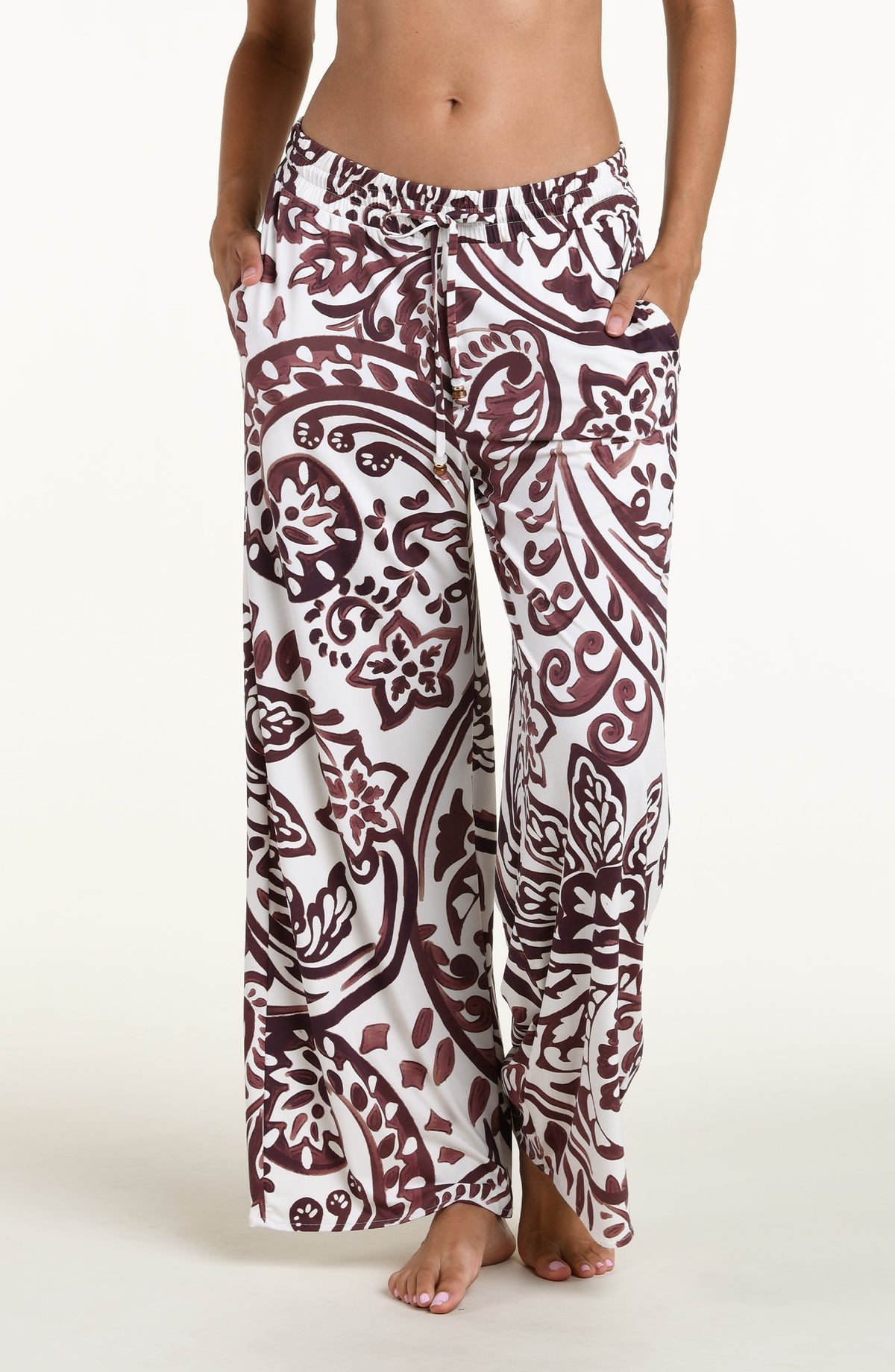 A person wearing loose, wide-leg pants with an allover paisley-style print in dark brown and white against a plain light background.