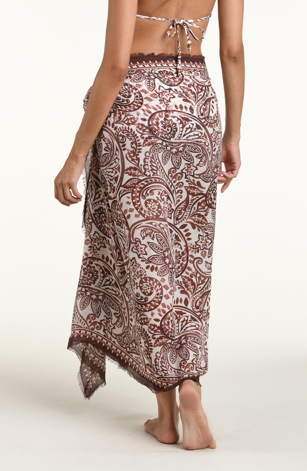 A woman wearing a brown and beige paisley-patterned sarong wrap against a plain light background.