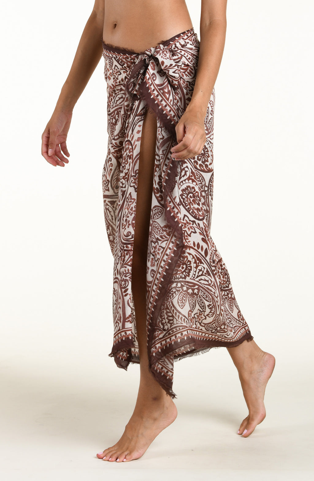 A woman wearing a brown and beige paisley-patterned sarong wrap against a plain light background.