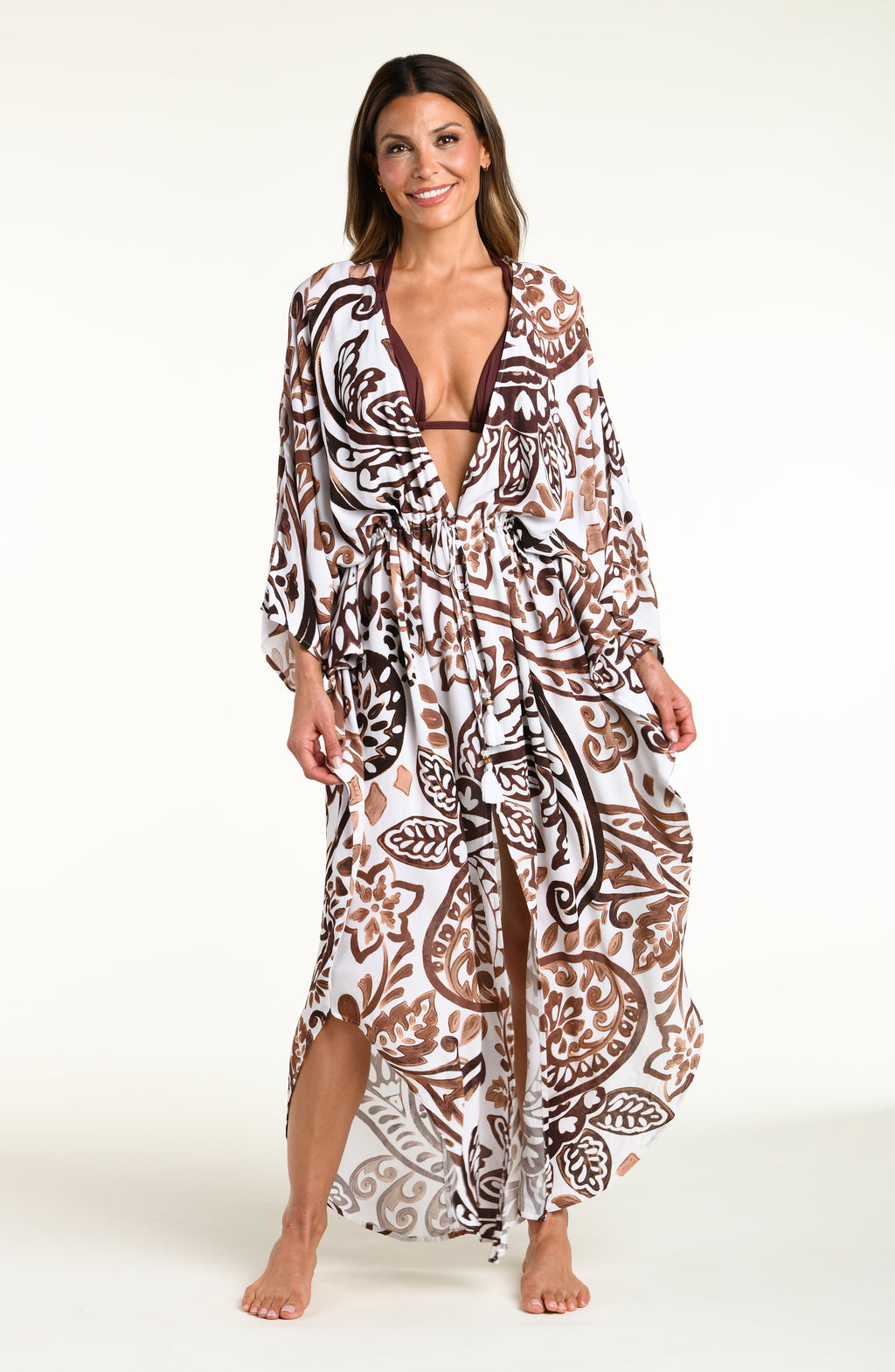 A woman modeling a long white caftan cover-up with a brown and white bohemian paisley pattern, standing against a plain white studio background.