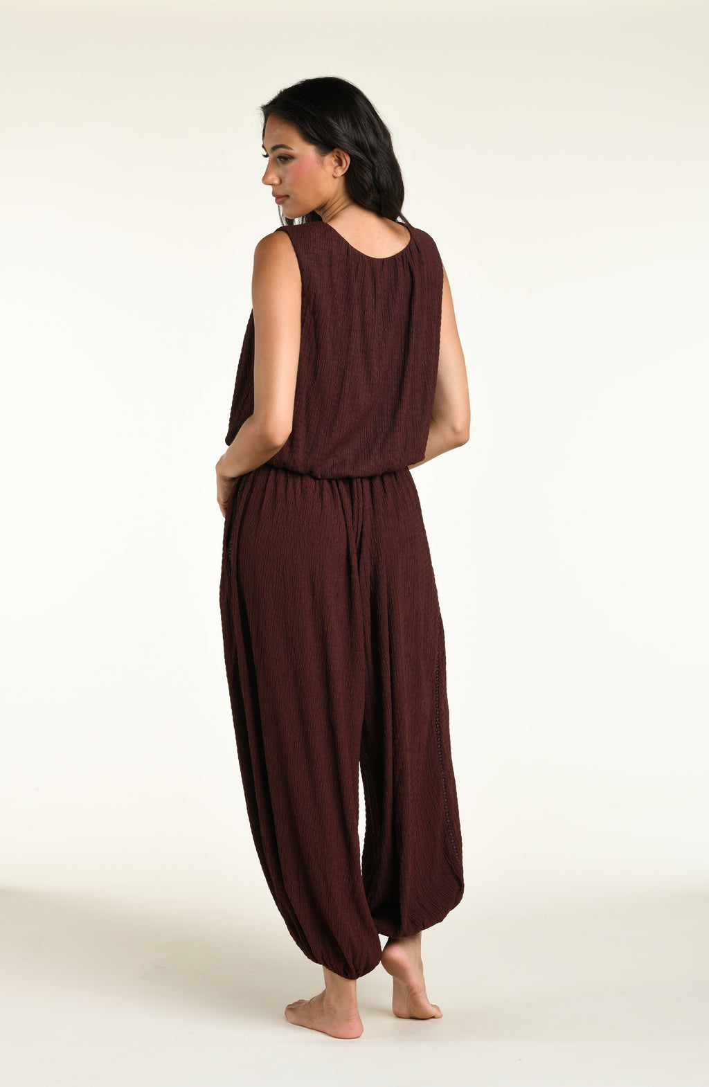 A woman wearing java brown colored crochet style pants and a matching sleeveless top against a white background. 