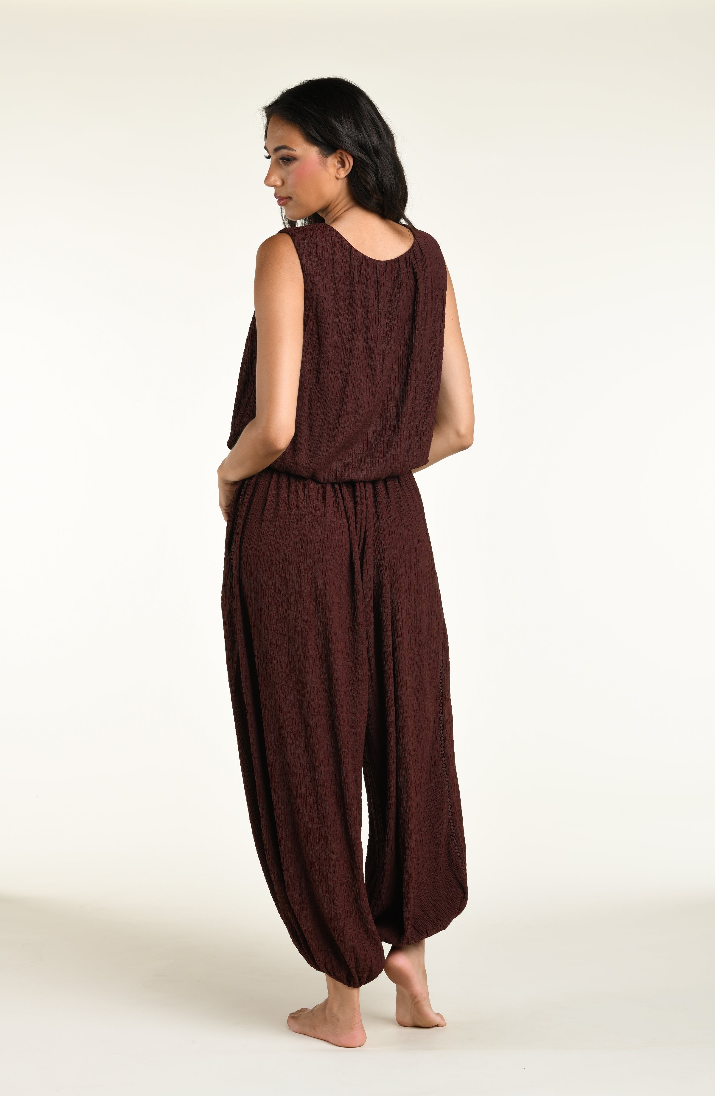 A woman wearing java brown colored crochet style pants and a matching sleeveless top against a white background. 