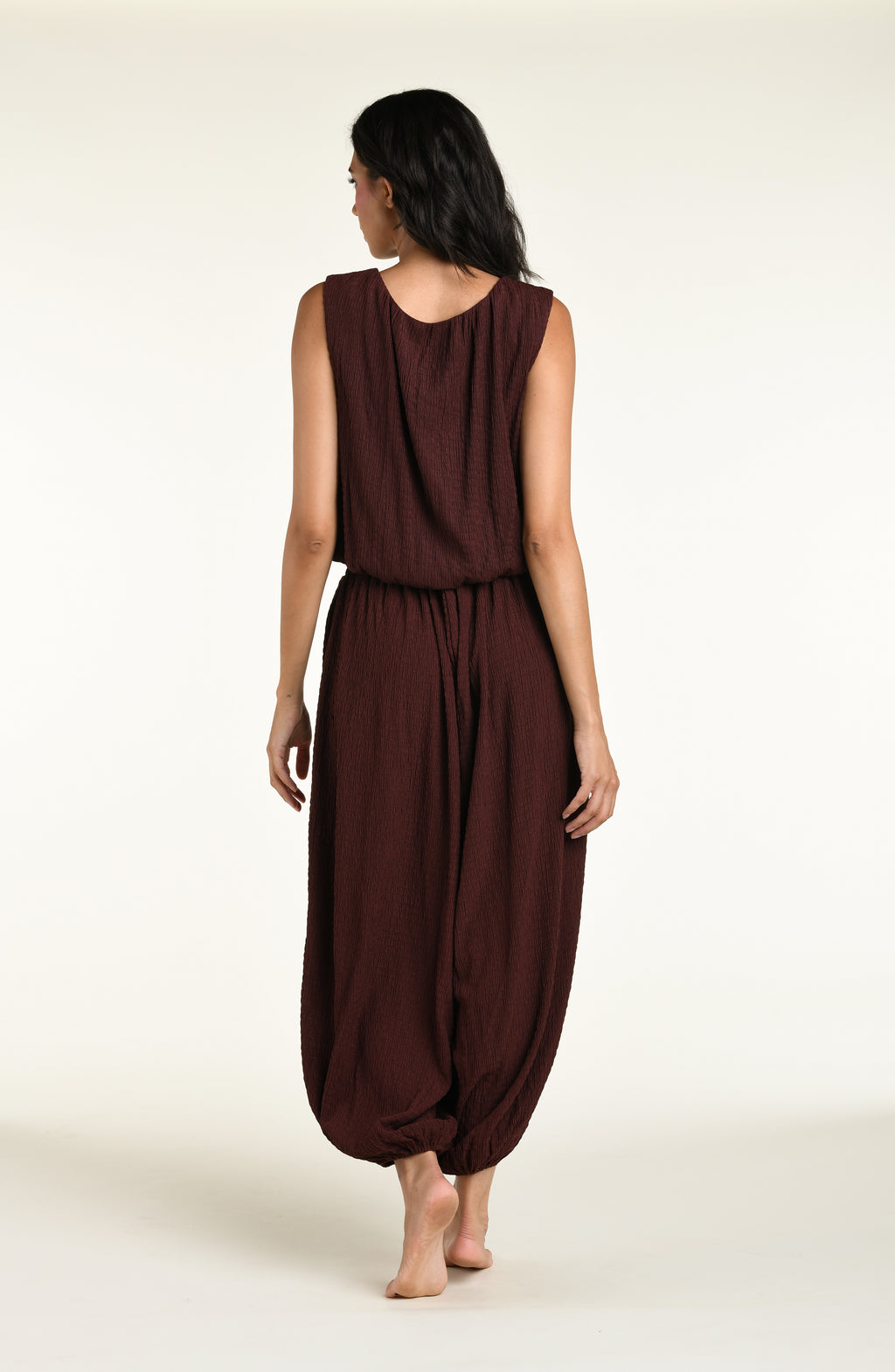 A woman wearing java brown colored crochet style pants and a matching sleeveless top against a white background. 