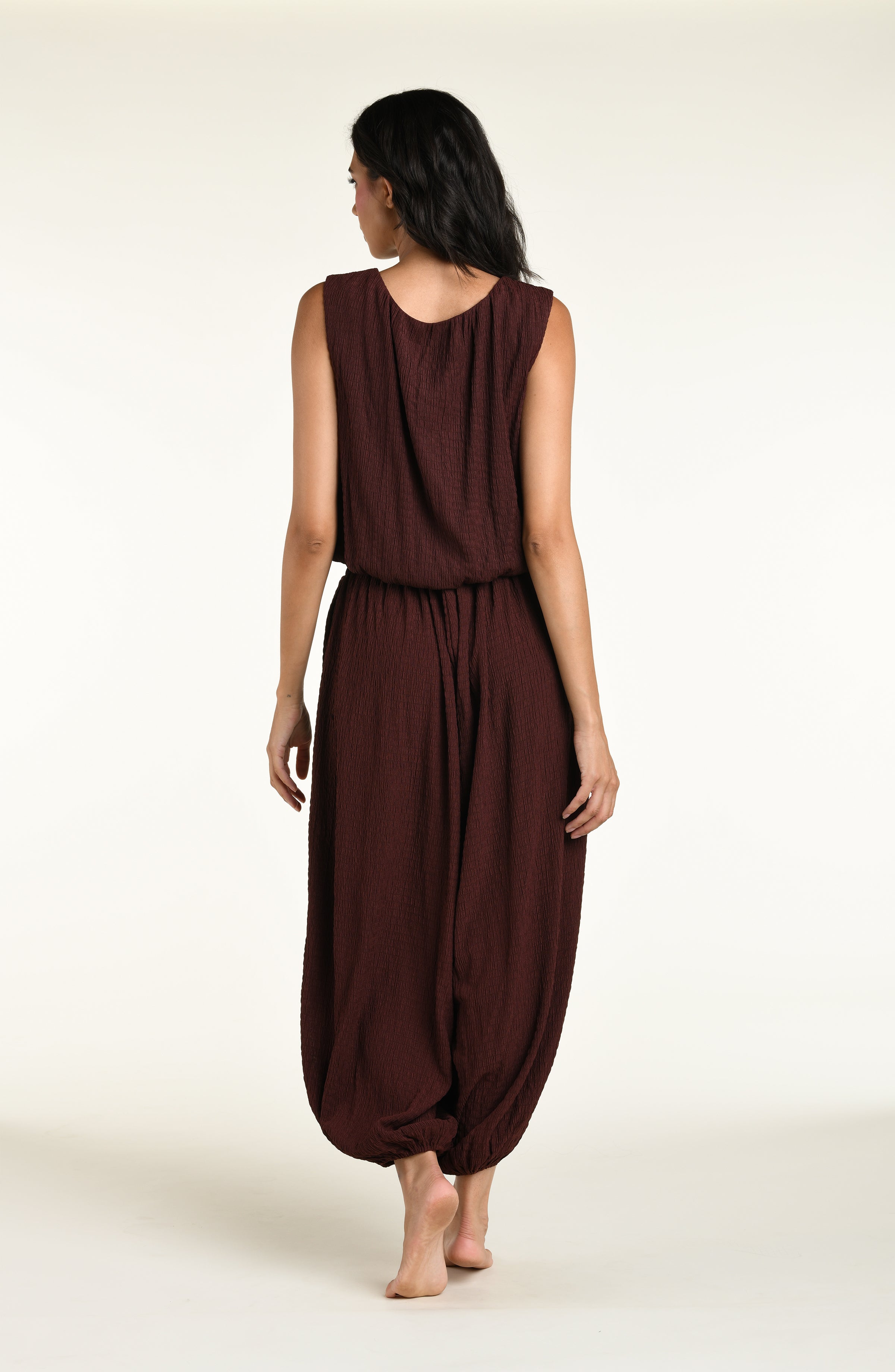 A woman wearing java brown colored crochet style pants and a matching sleeveless top against a white background. 