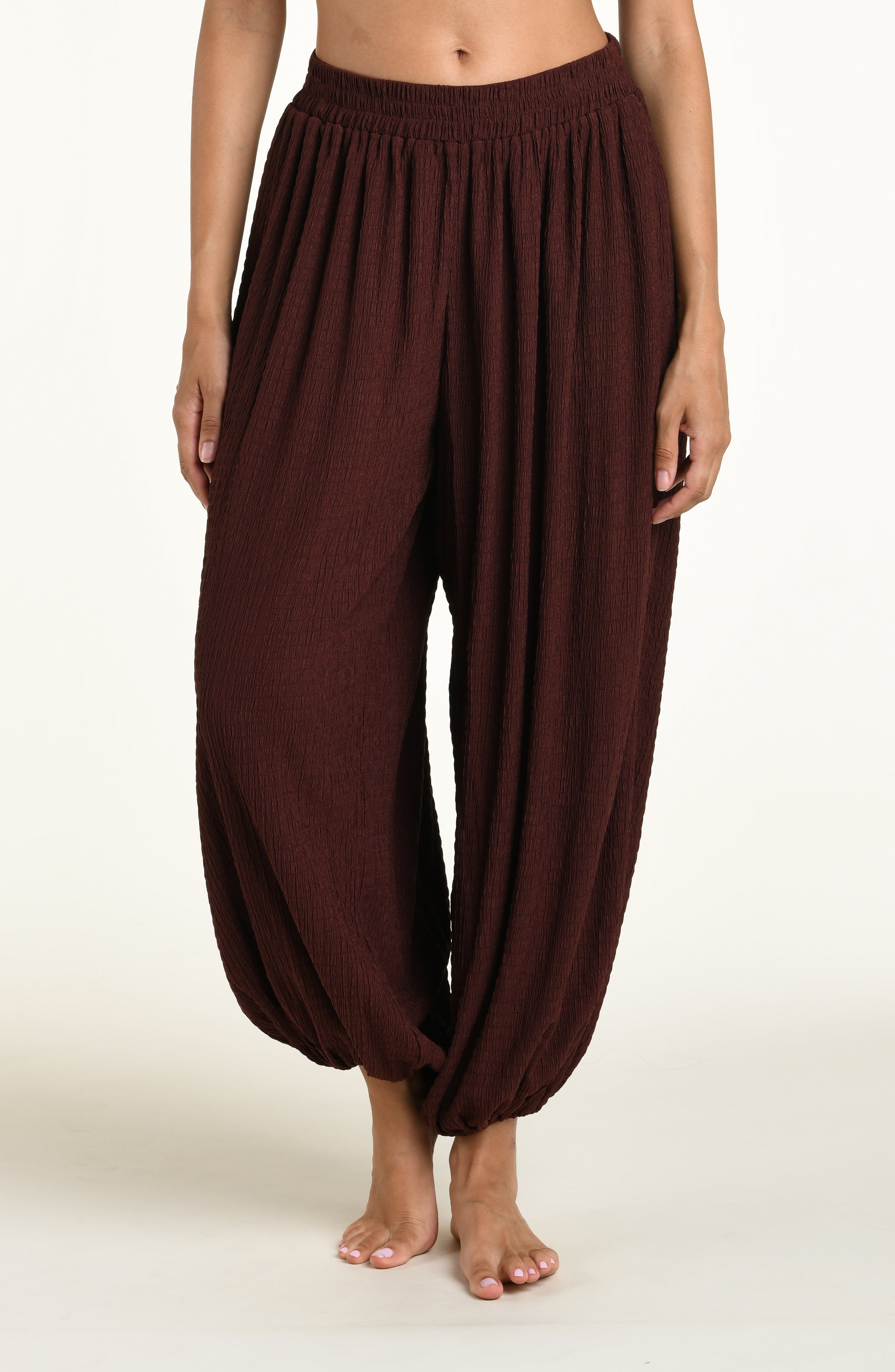 A woman wearing java brown colored crochet style pants against a white background. 