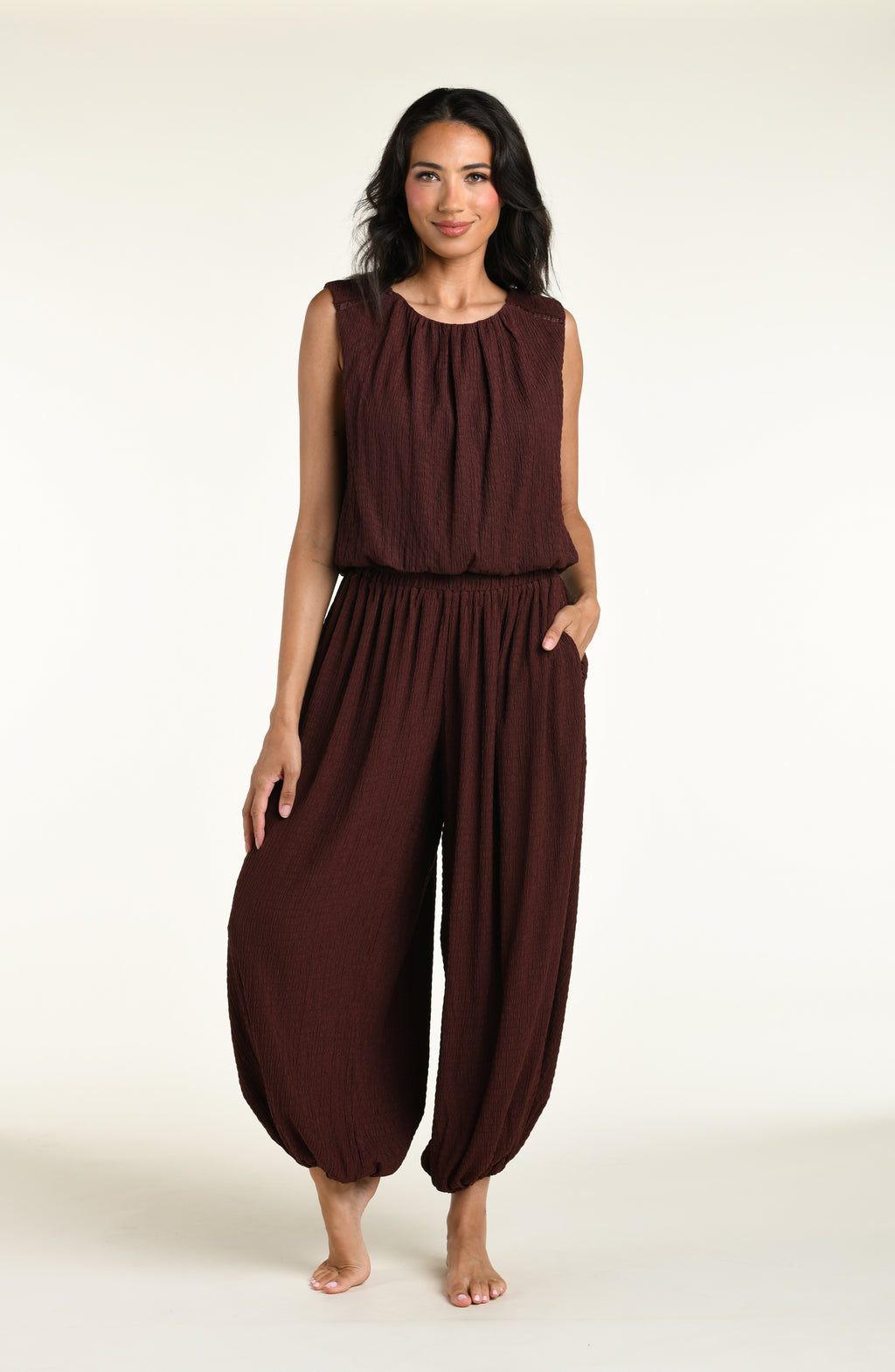 A woman wearing java brown colored crochet style pants and a matching sleeveless top against a white background. 