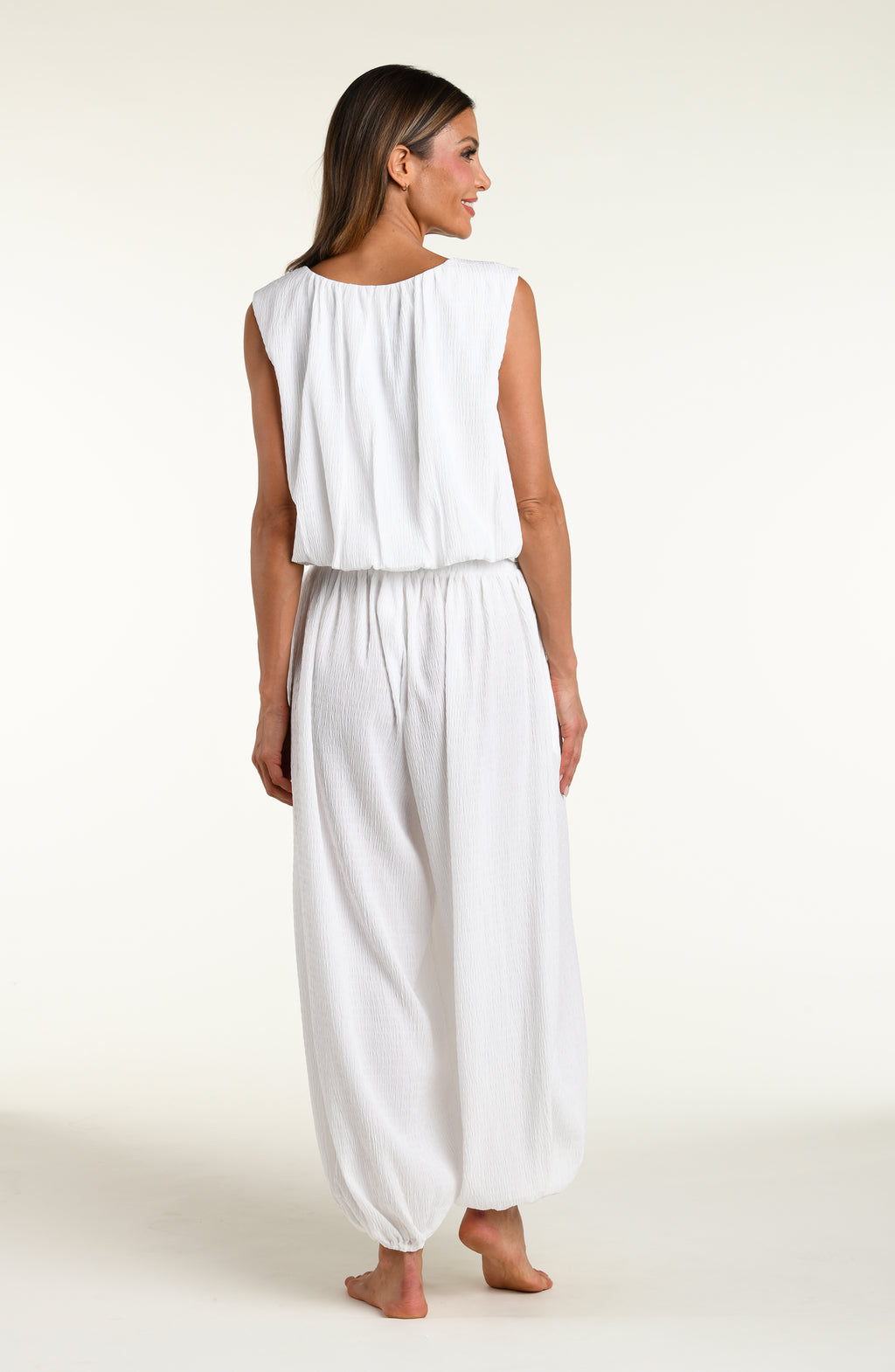 Woman wearing white crochet style beach pants and matching sleeveless top against a white background. 