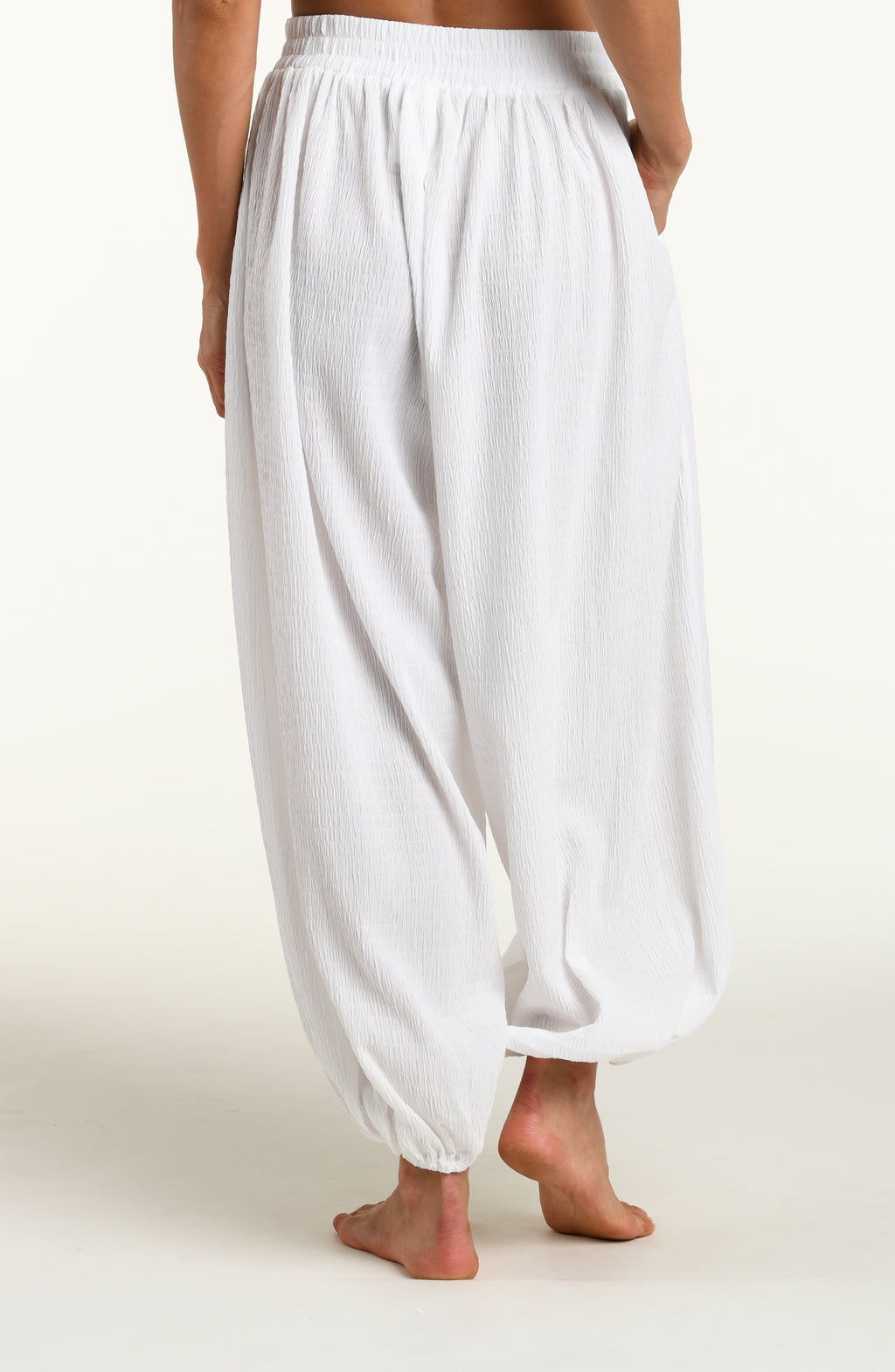 Woman wearing white crochet style beach pants against a white background. 
