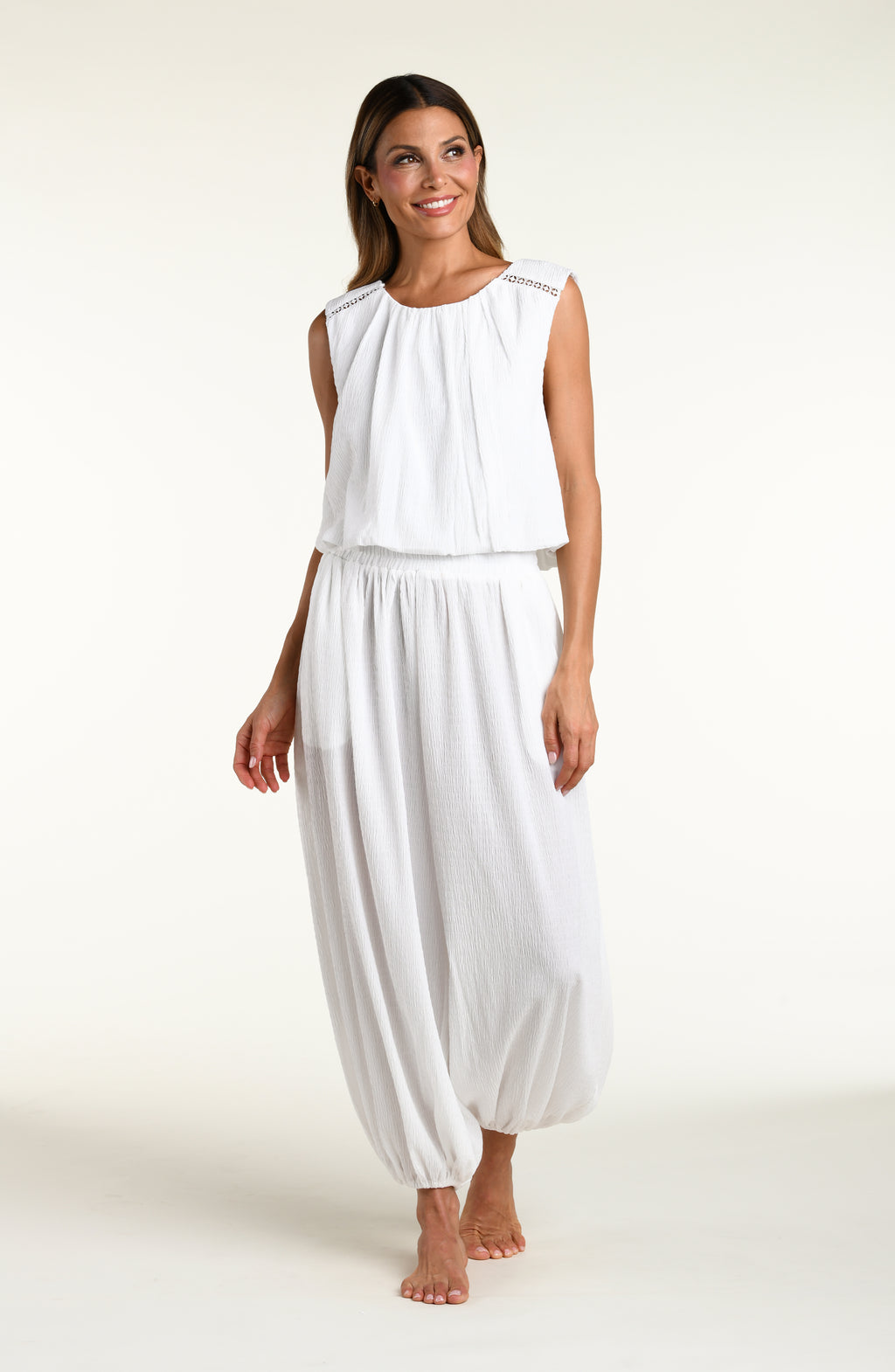 Woman wearing white crochet style beach pants and matching sleeveless top against a white background. 